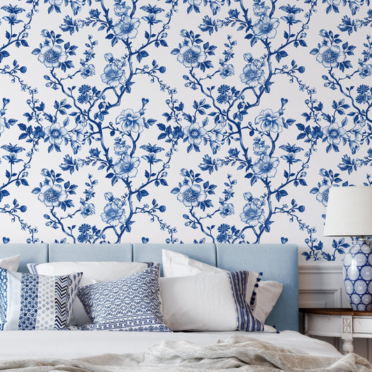 a bedroom with a blue and white floral wallpaper on the wall behind a bed with white pillows and a blue headboard.