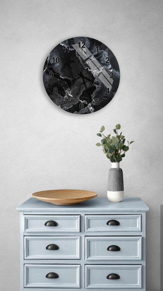 a wall clock with a black and white design, mounted on a wall above a light blue dresser with six drawers. The dresser also has a wooden bowl and a vase with greenery on it.