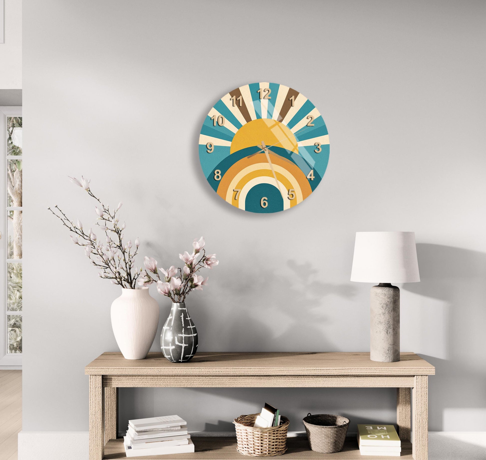 a wall clock with a sunburst design, a wooden table with a lamp, a vase with flowers, and some books on a shelf.