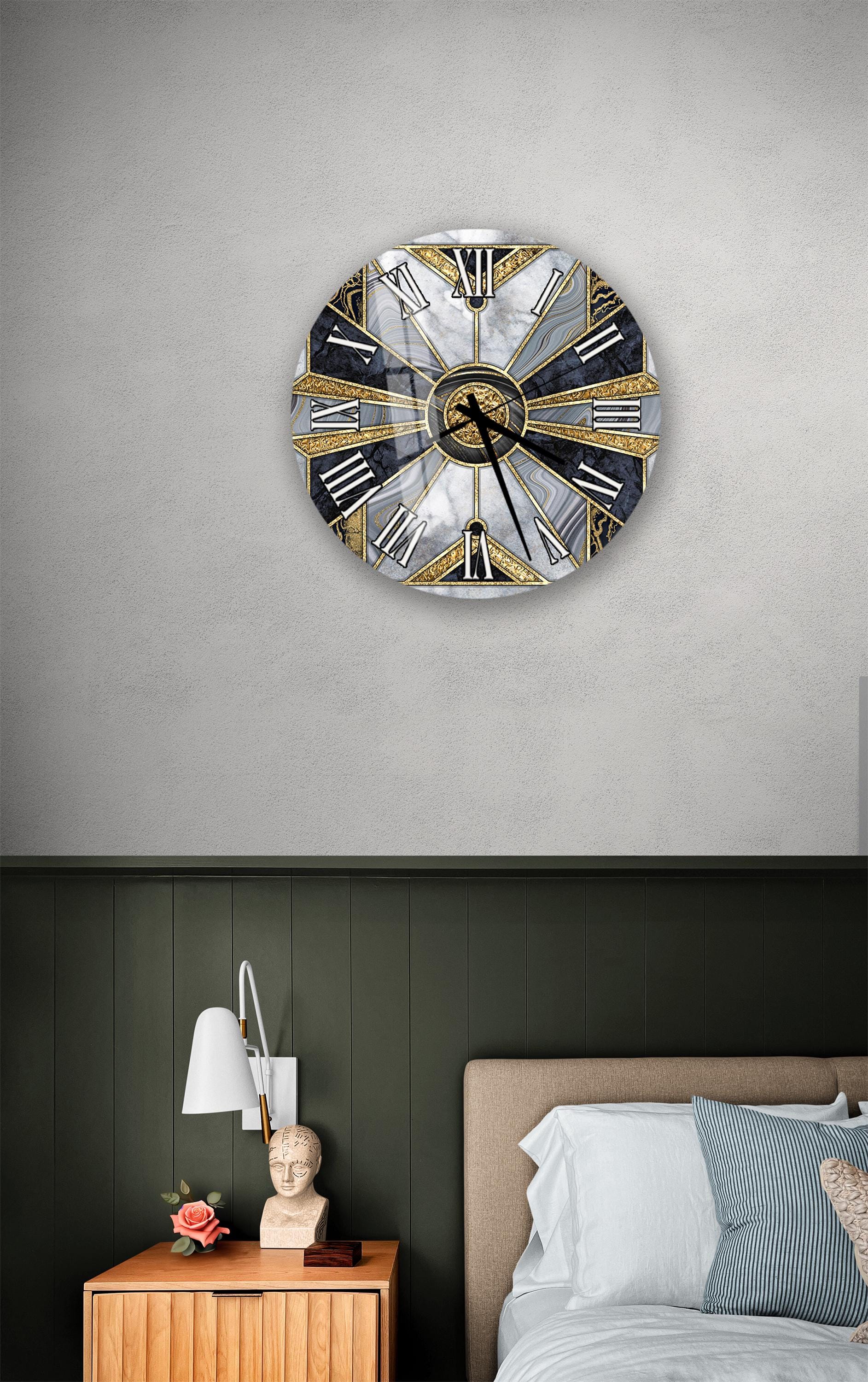 a bedroom setting with a large, ornate wall clock as the focal point. The clock has a gold and black design with Roman numerals. Below the clock, there is a wooden nightstand with a lamp and a small statue. The bed is covered with white sheets and has a blue and white striped pillow. The walls are painted in a dark green color, and the overall scene has a modern and stylish aesthetic.
