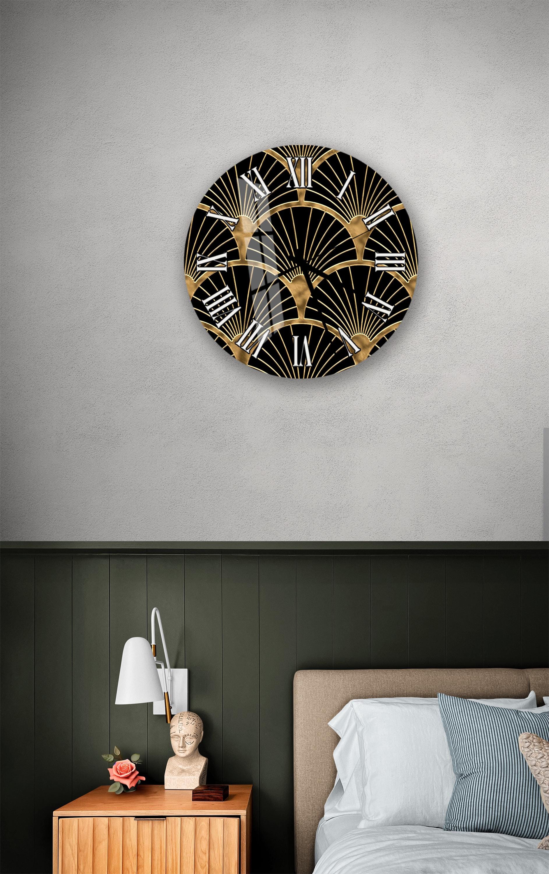 a bedroom setting with a large circular wall clock displaying an Art Deco pattern in gold and black. The clock is mounted on a wall above a bed with a wooden headboard. The room also includes a nightstand with a lamp and a small statue.