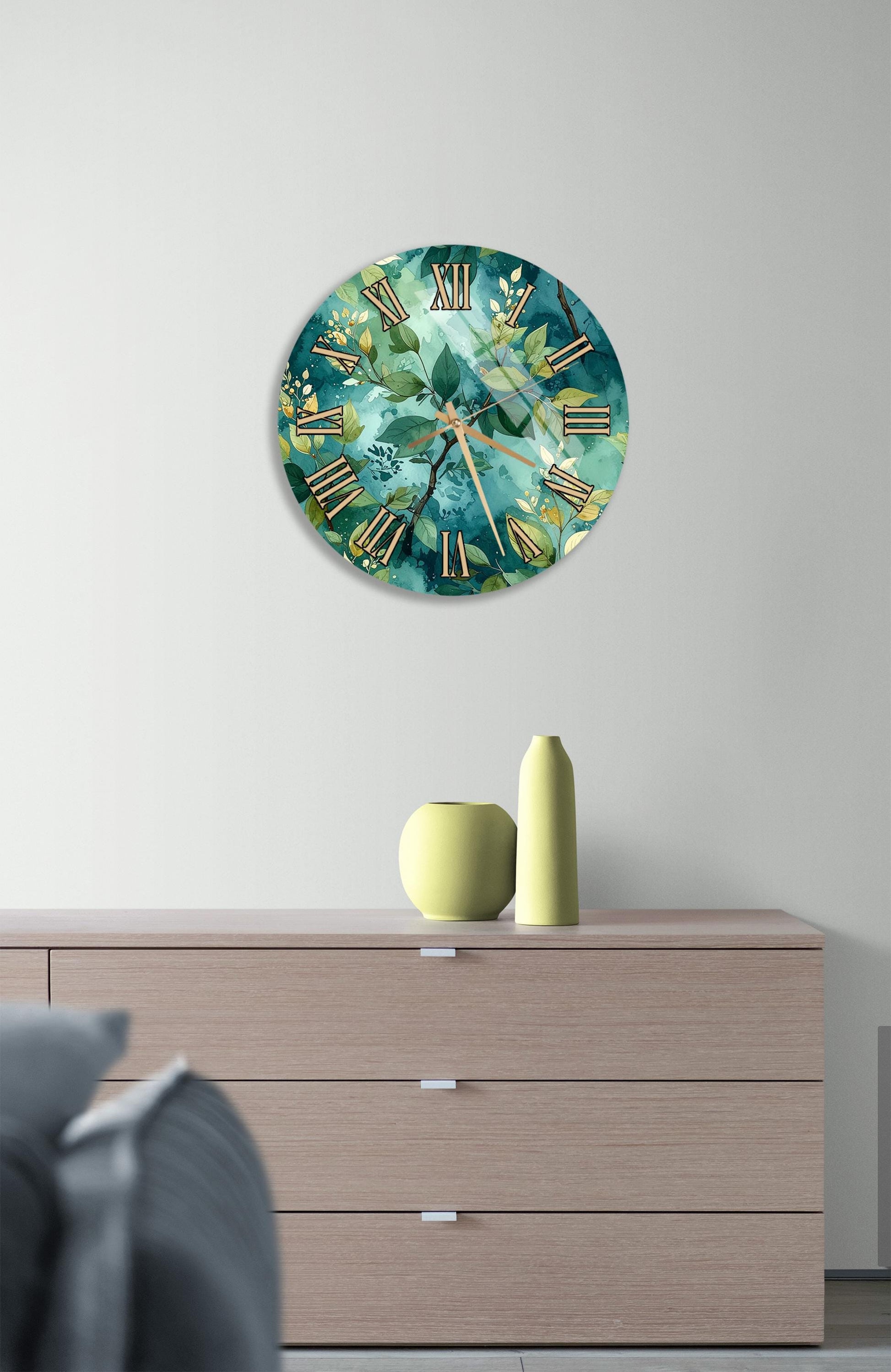 a wall clock with a green and blue floral design, mounted on a wall above a wooden dresser with three drawers.