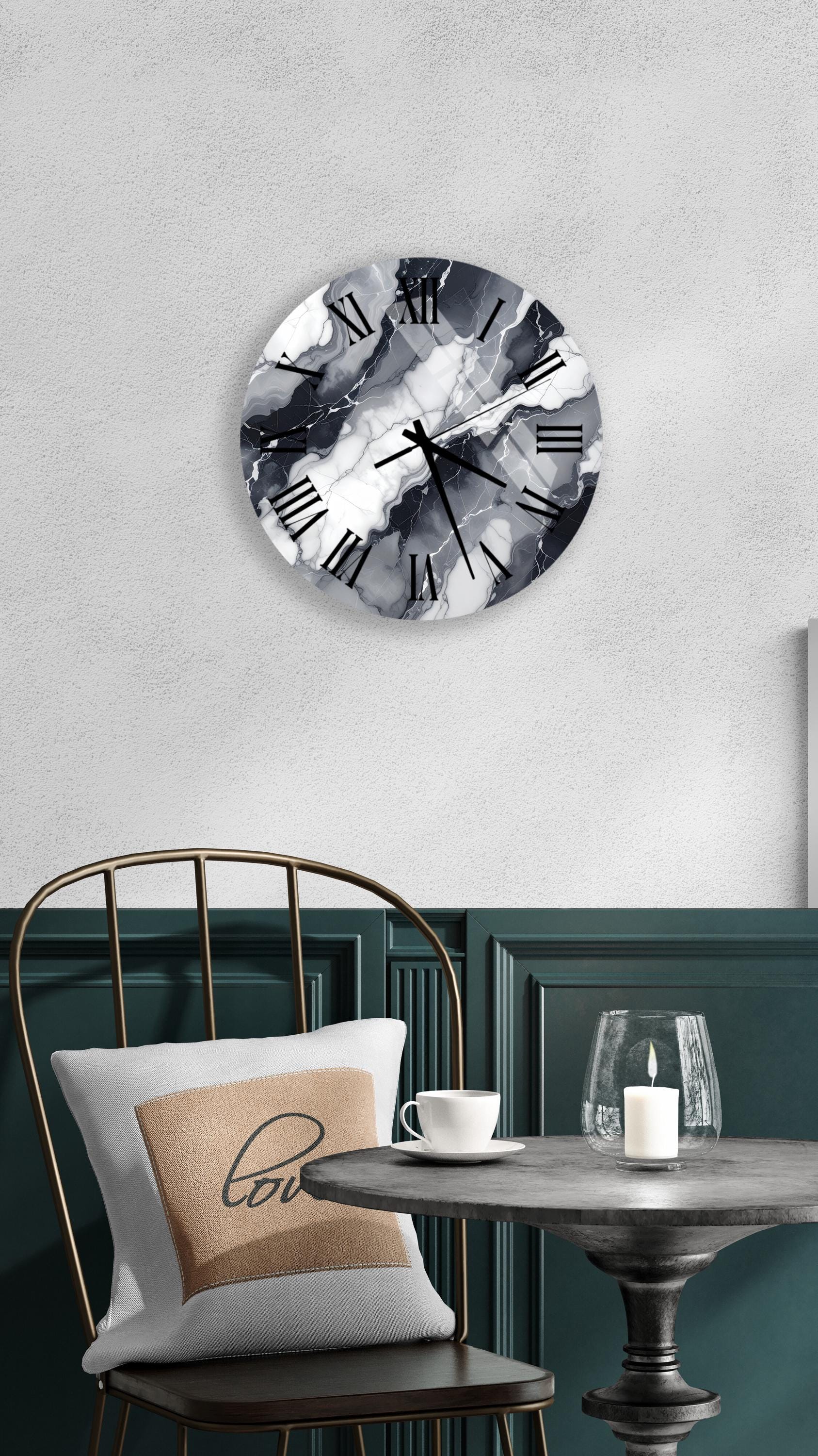 a modern black and white clock with a marble-like design, mounted on a wall above a table with a white tablecloth. The table has a candle and a cup on it, creating a cozy and inviting atmosphere.