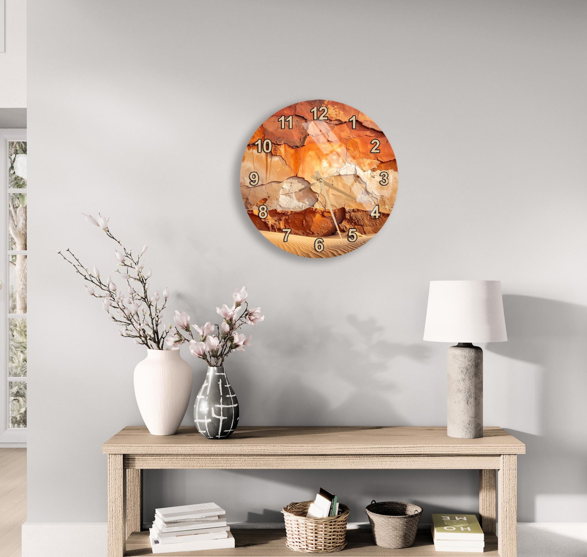 a wall clock with an abstract design, a wooden table with a lamp, a vase with flowers, and some books on a shelf.