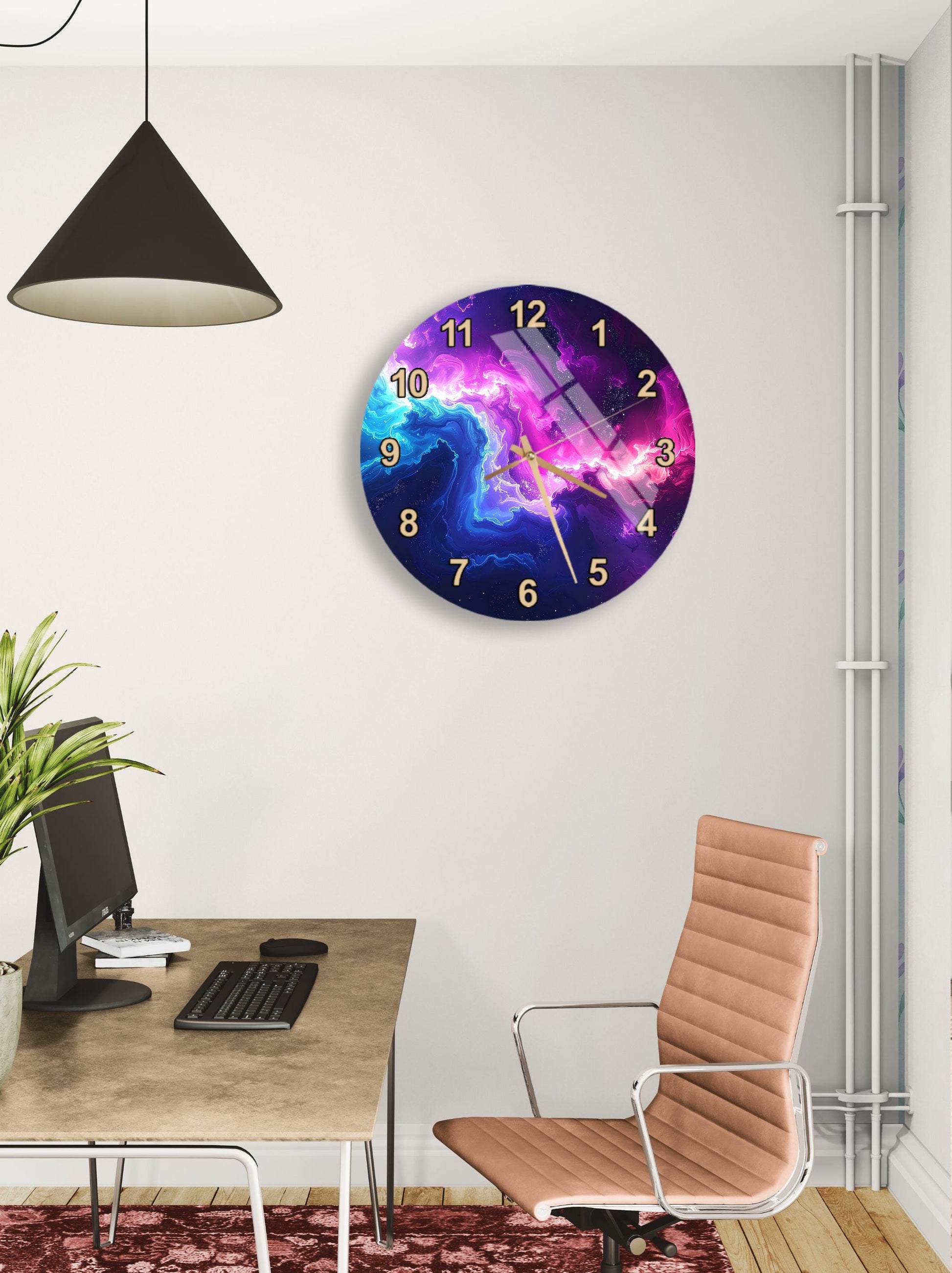 a modern office space with a large wall clock displaying a colorful space-themed design. The clock is mounted on the wall above a desk with a computer monitor, keyboard, and mouse. A comfortable-looking chair is positioned in front of the desk, and a potted plant is visible in the background.