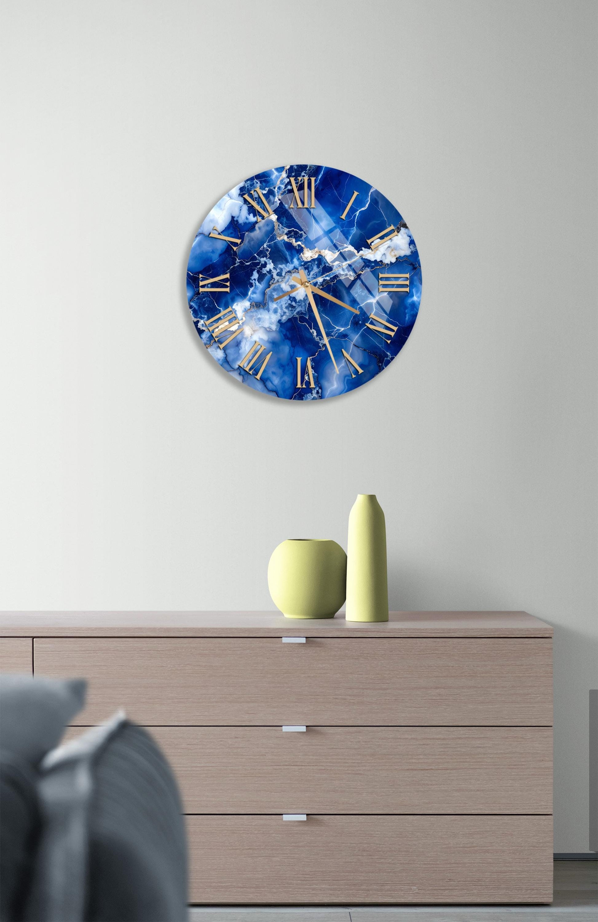 a wall clock with a blue and white marble design, mounted on a wall above a wooden dresser with three drawers.
