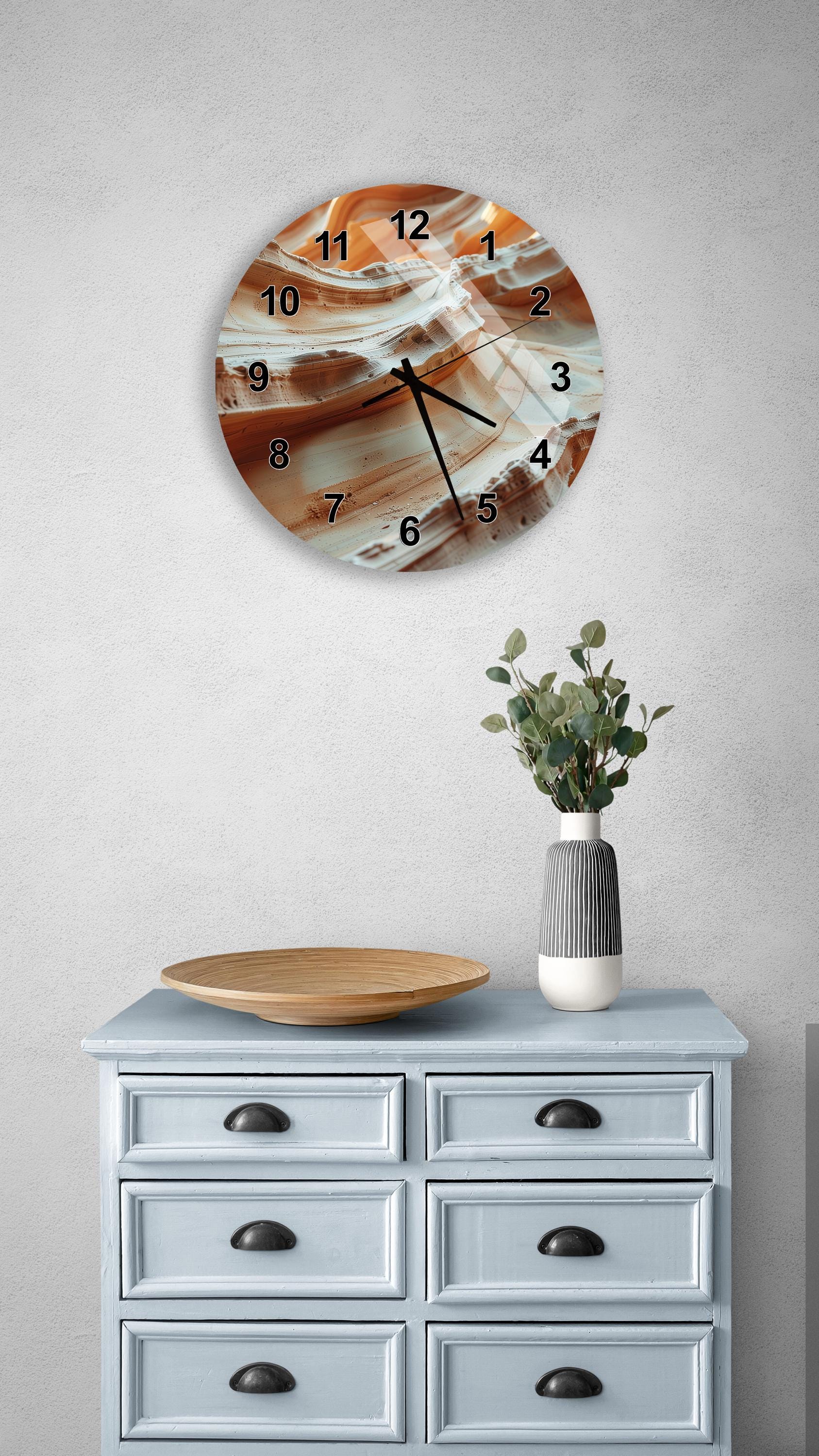 a wall clock with a unique abstract design, mounted on a wall above a light blue wooden dresser with six drawers. The dresser also has a vase with greenery on it, and a wooden plate on top.