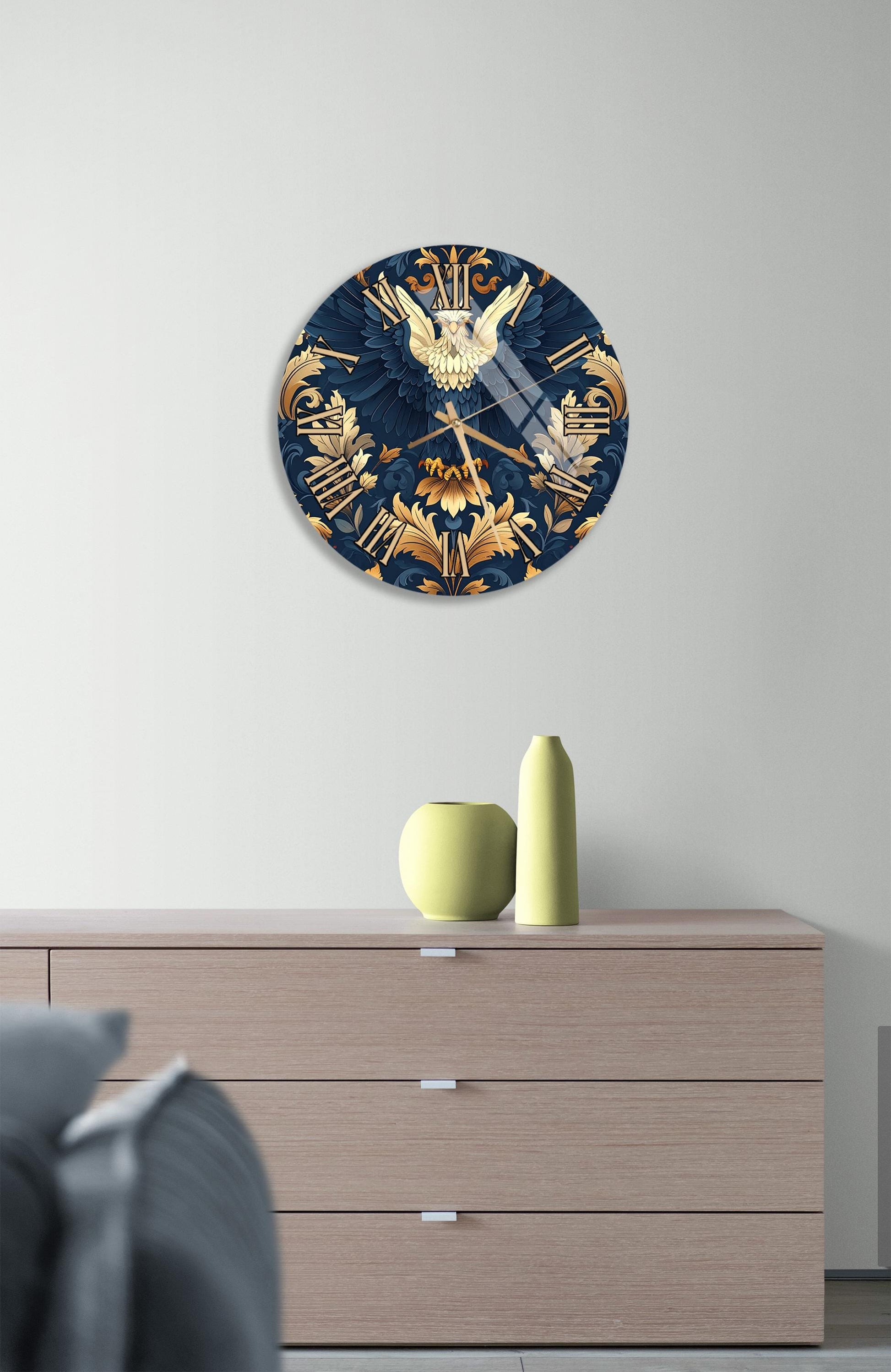 a wall clock with a blue and gold design, mounted on a wall above a wooden dresser with a vase and a small sculpture on top.