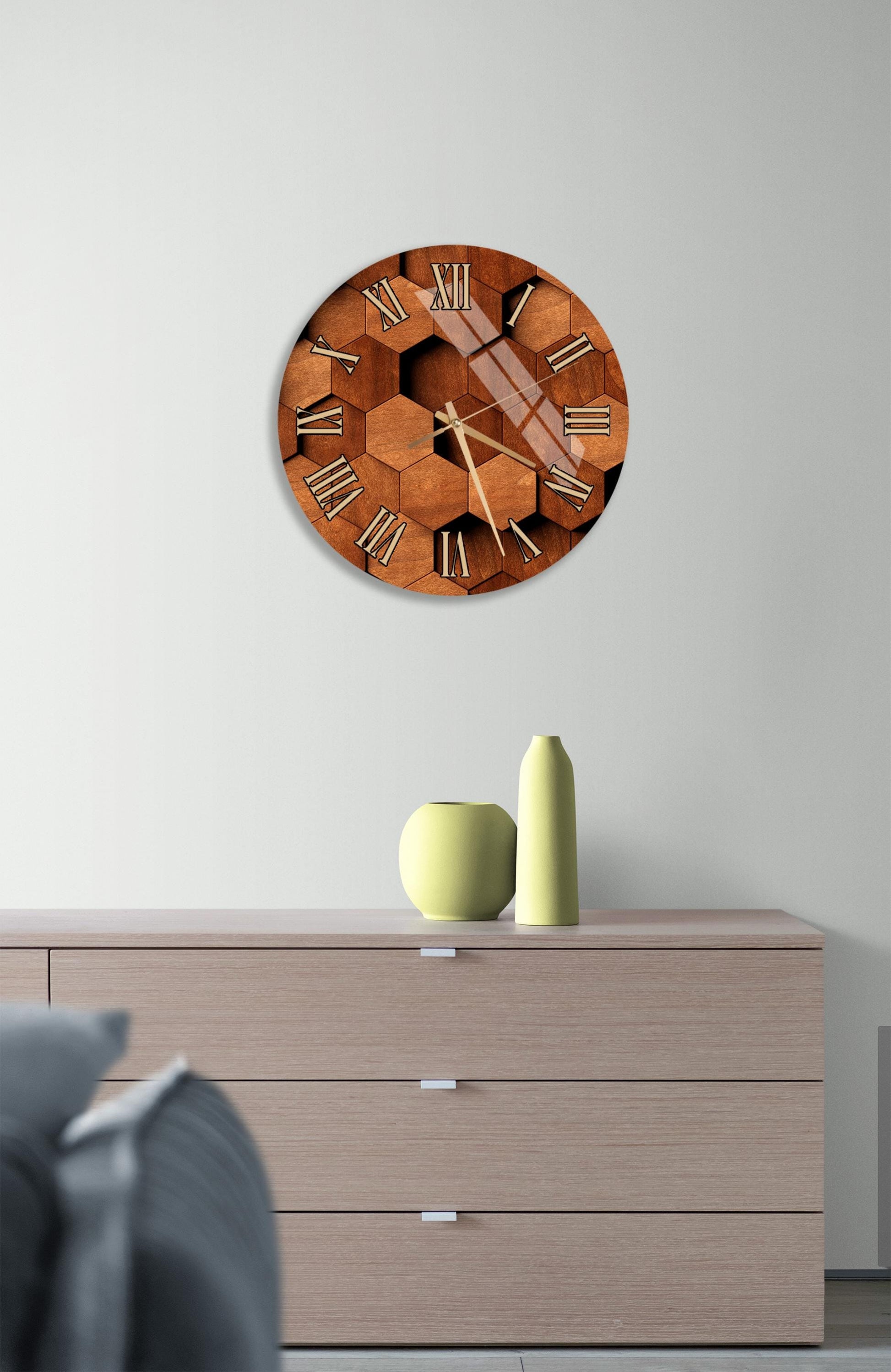 a wooden clock with a hexagonal design on a white wall, mounted above a wooden dresser with a vase and a small green pot on top.