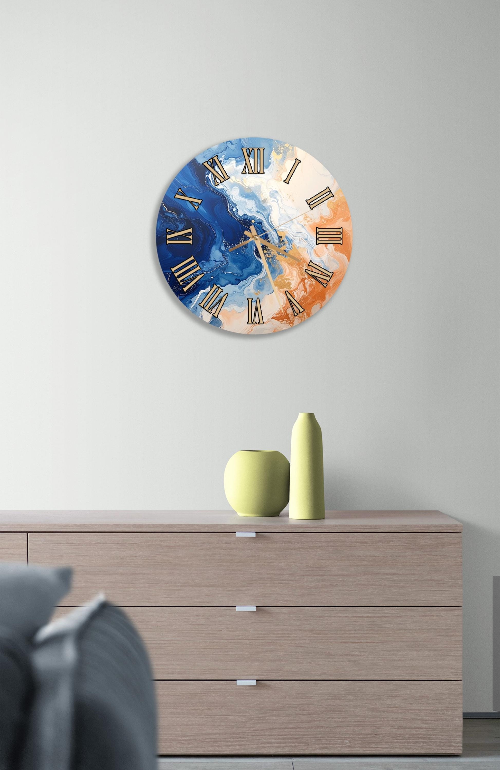 a wall clock with a marble-like design, mounted on a wall above a wooden dresser. The dresser has a vase and a small sculpture on top of it.