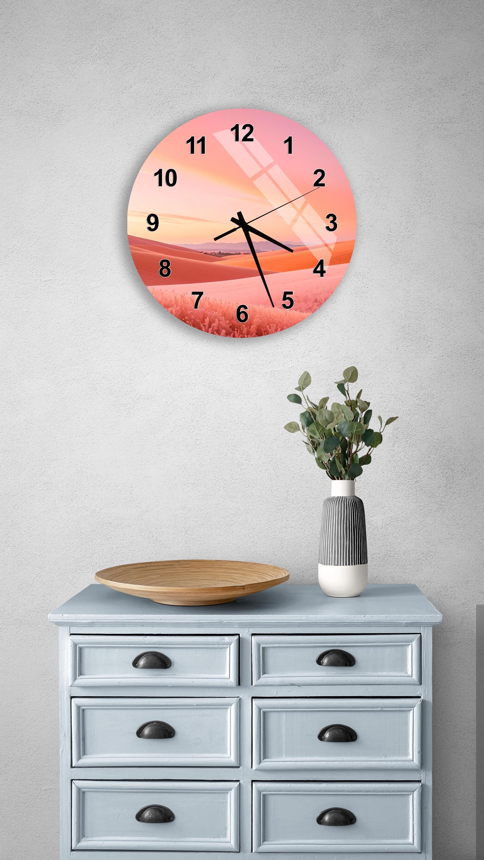 a wall clock with a sunset landscape design, mounted on a wall above a wooden dresser with drawers.
