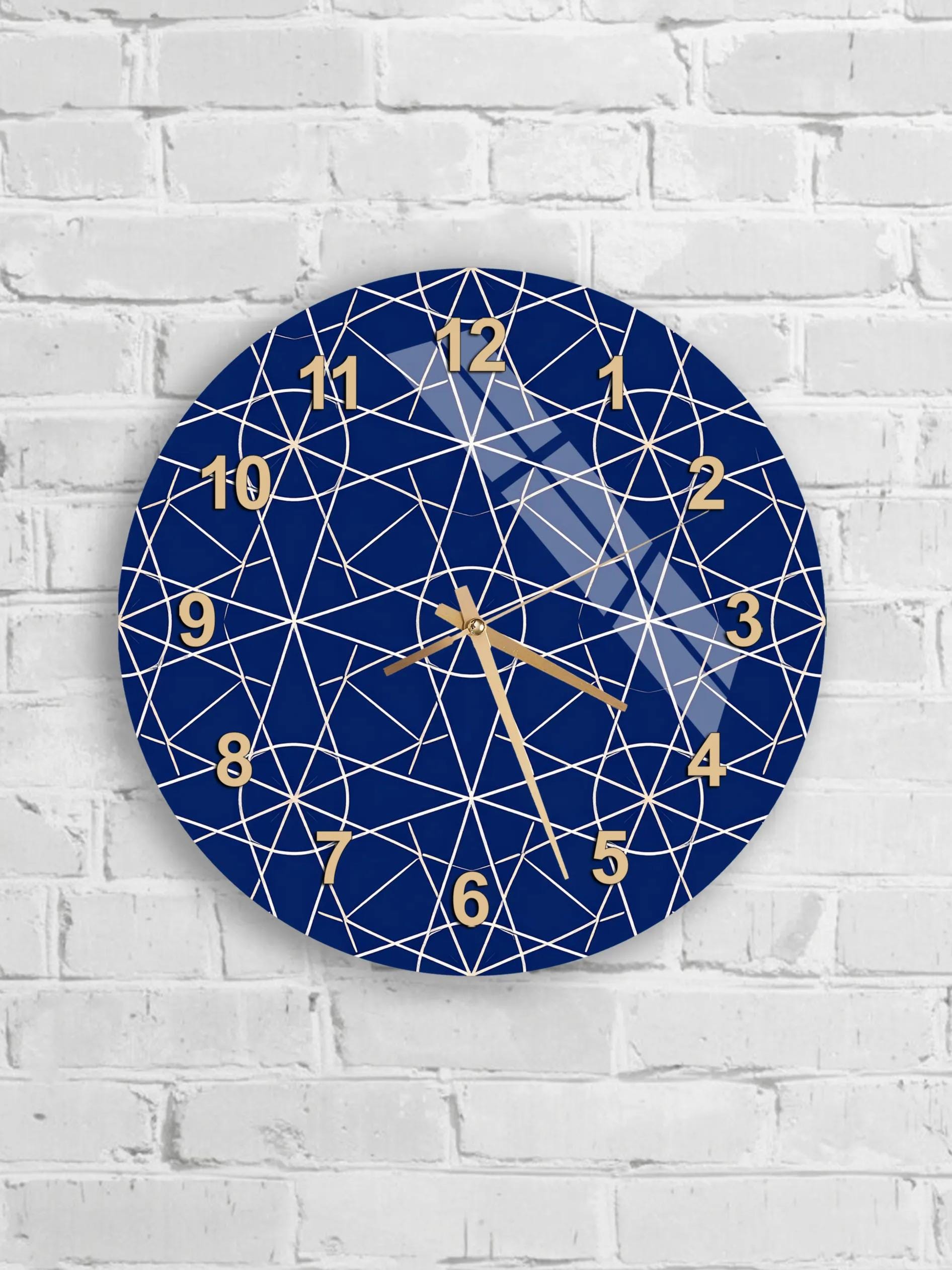 A blue wall clock with a geometric pattern and gold hands is mounted on a white brick wall.