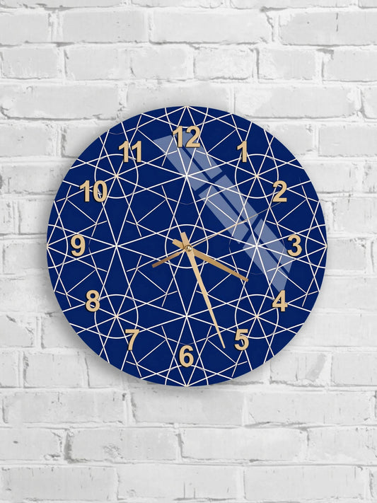 A blue wall clock with a geometric pattern and gold hands is mounted on a white brick wall.