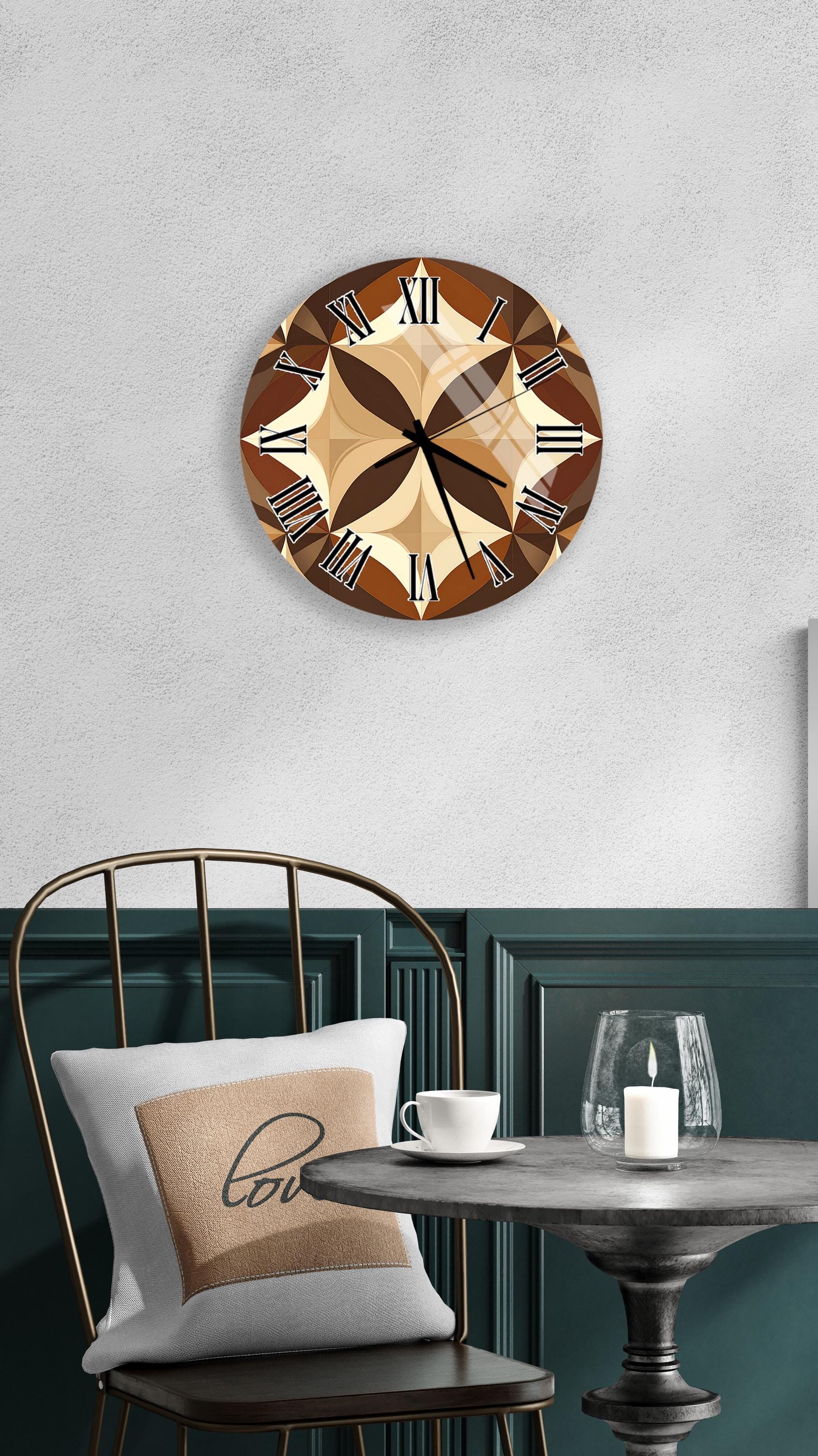 a wall clock with a brown and beige design, mounted on a wall above a table with a white tablecloth. The table has a glass candle holder and a white coffee cup on it. A white pillow with the word "love" printed on it is also present on the table.