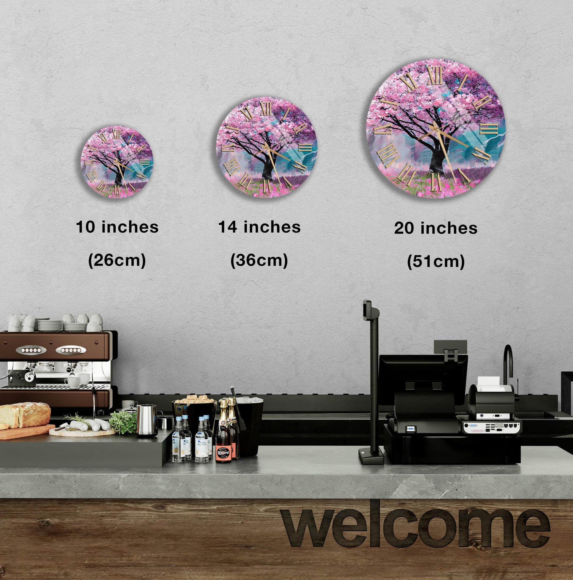 A wall clock with a tree design is displayed on a wall, accompanied by three different sizes of the same clock. Below the clock, there is a counter with various items such as bottles and a sandwich. The word "welcome" is written on the counter.