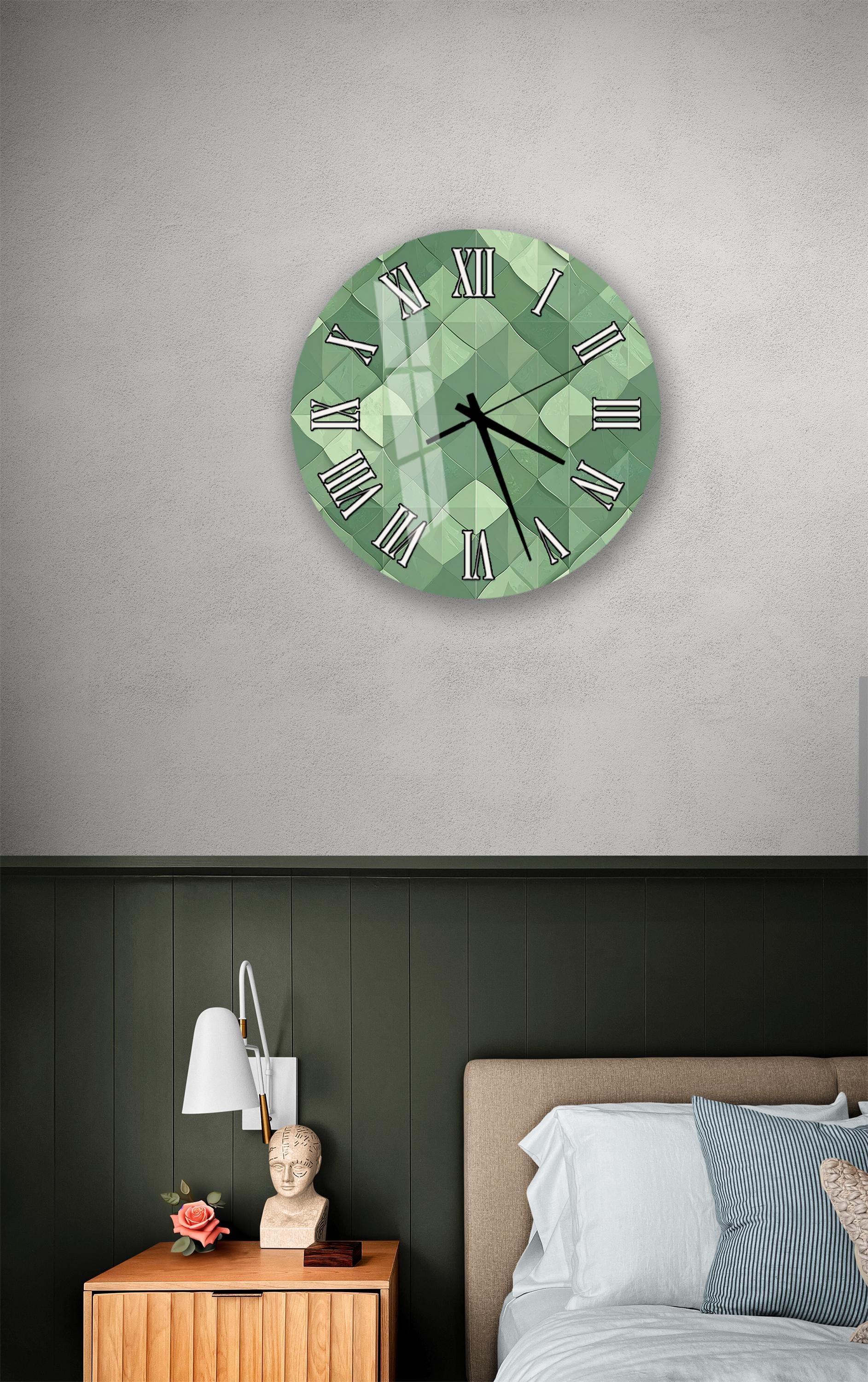 a bedroom setting with a large green clock on the wall above a bed. The clock has a geometric design and Roman numerals. The room has a dark green wall, a wooden nightstand with a lamp, and a white headboard.