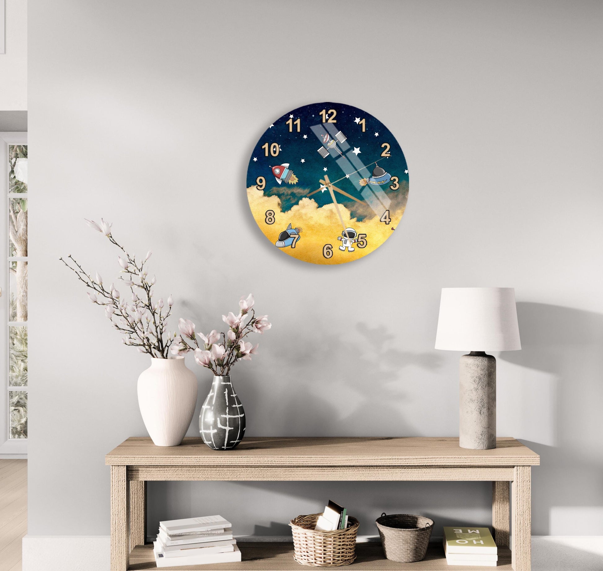 a wall clock with a space theme, a wooden table with a lamp, a vase with flowers, and some books on a shelf.