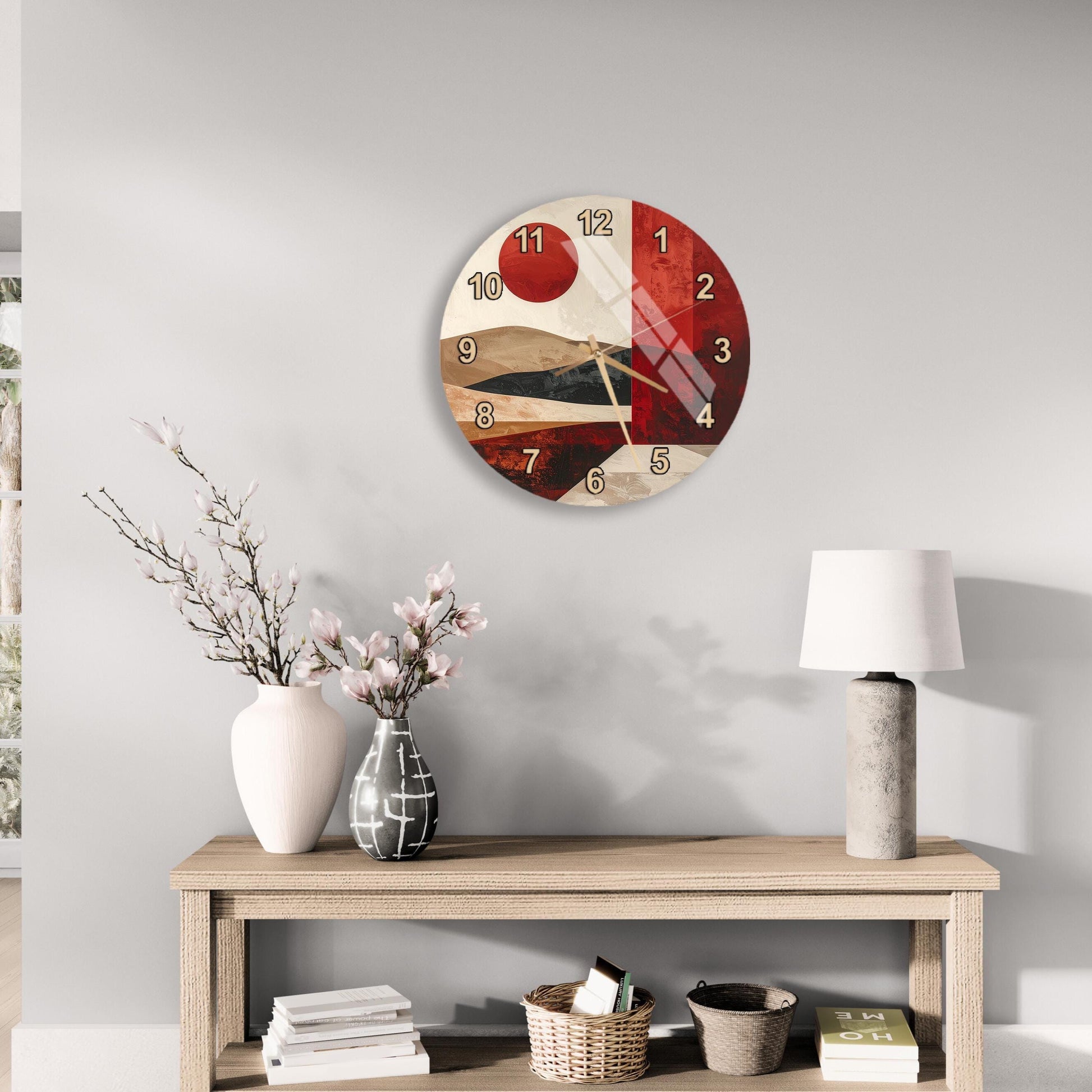 a wall clock with a red and white design, a wooden table with a lamp, a vase with flowers, and some books on a shelf.