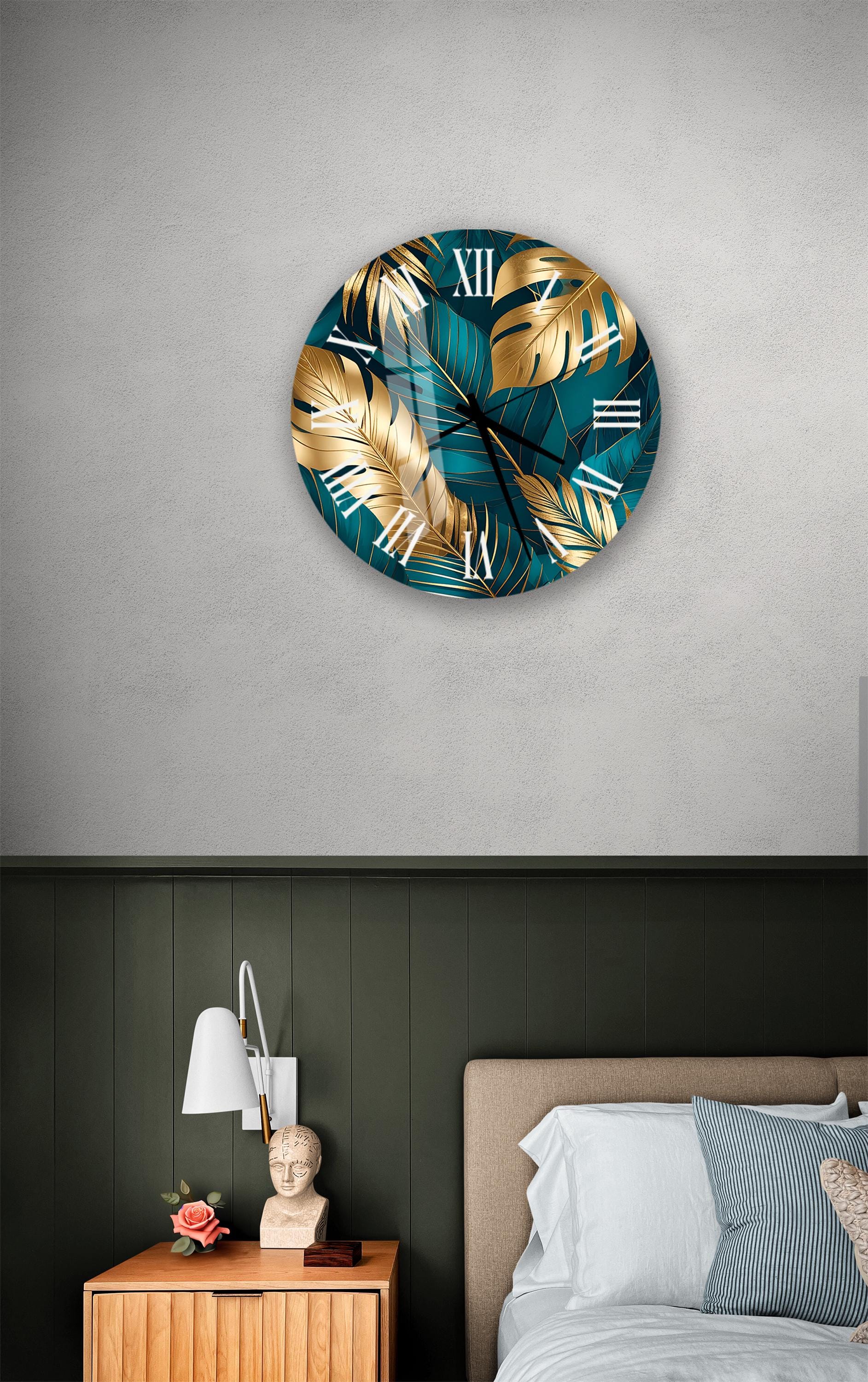 a bedroom setting with a large wall clock displaying a tropical leaf pattern in shades of blue and gold. The clock is mounted on a wall above a bed with a white headboard. The room also includes a nightstand with a lamp and a small statue.