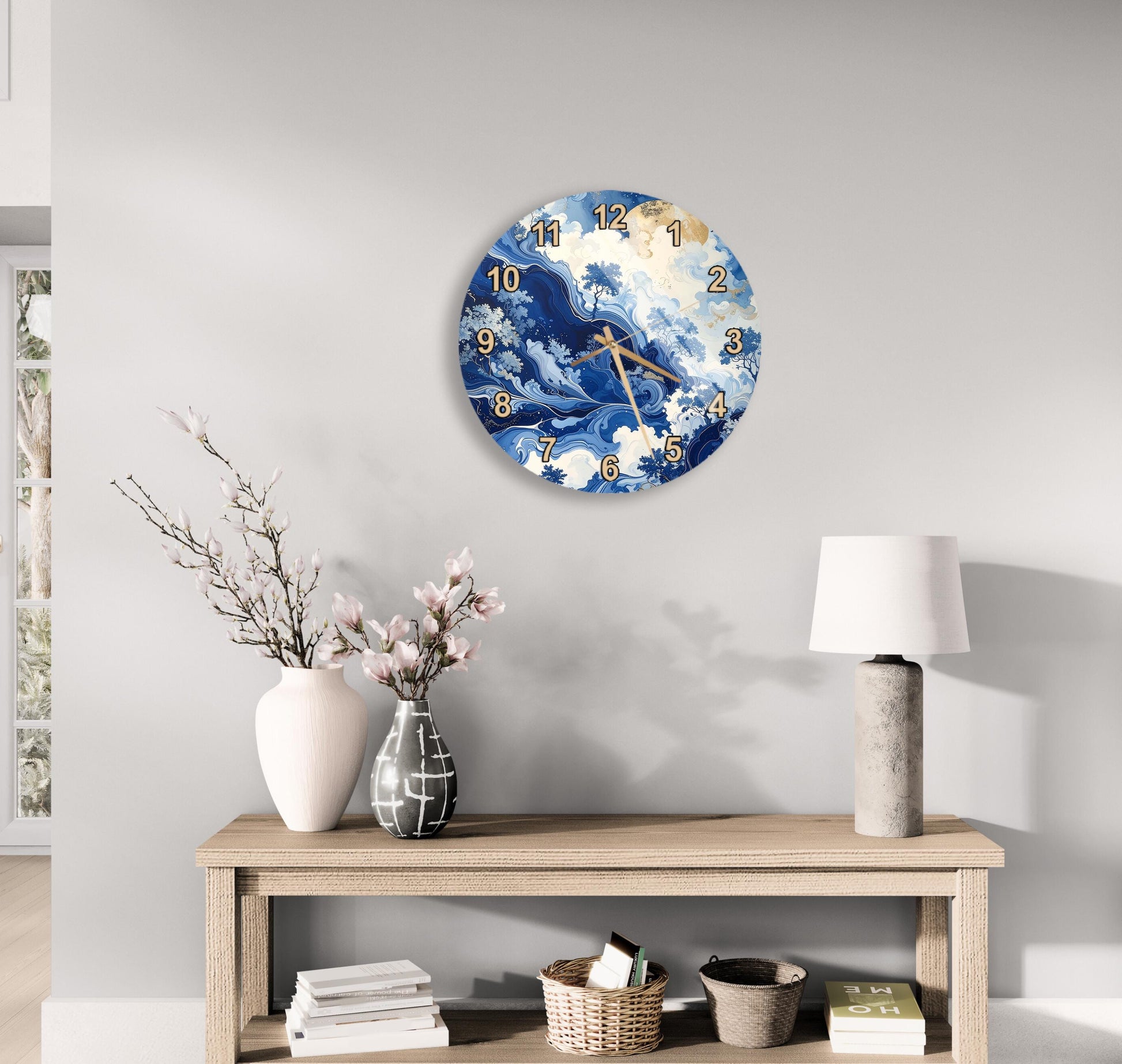 a wall clock with a blue and white ocean wave design, a wooden table with a lamp, a vase with pink flowers, and a stack of books.