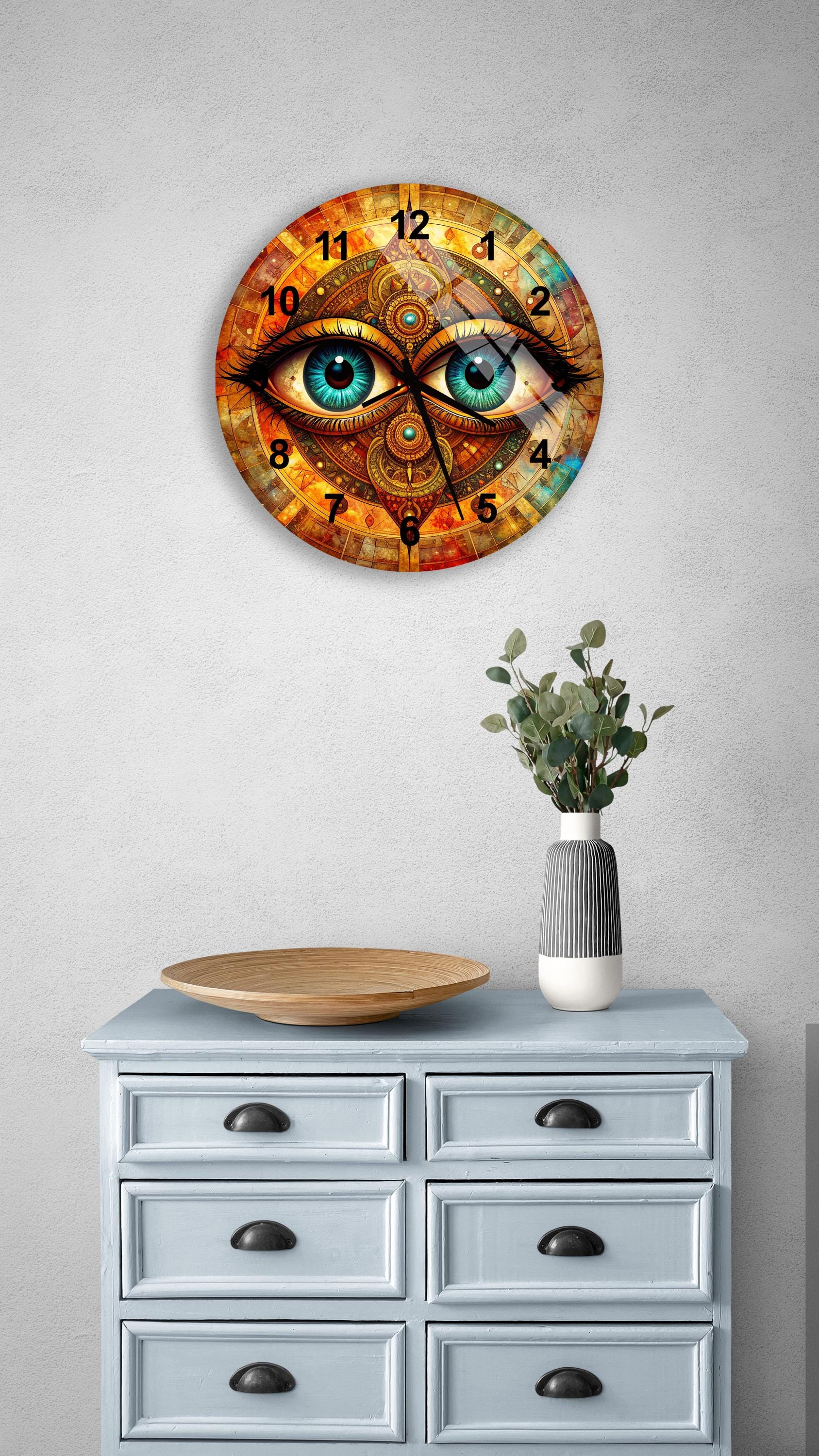 a wall clock with a unique design, depicting a pair of eyes on the clock face. The clock is mounted on a wall above a wooden dresser with six drawers. The dresser also has a vase and a plate on it.