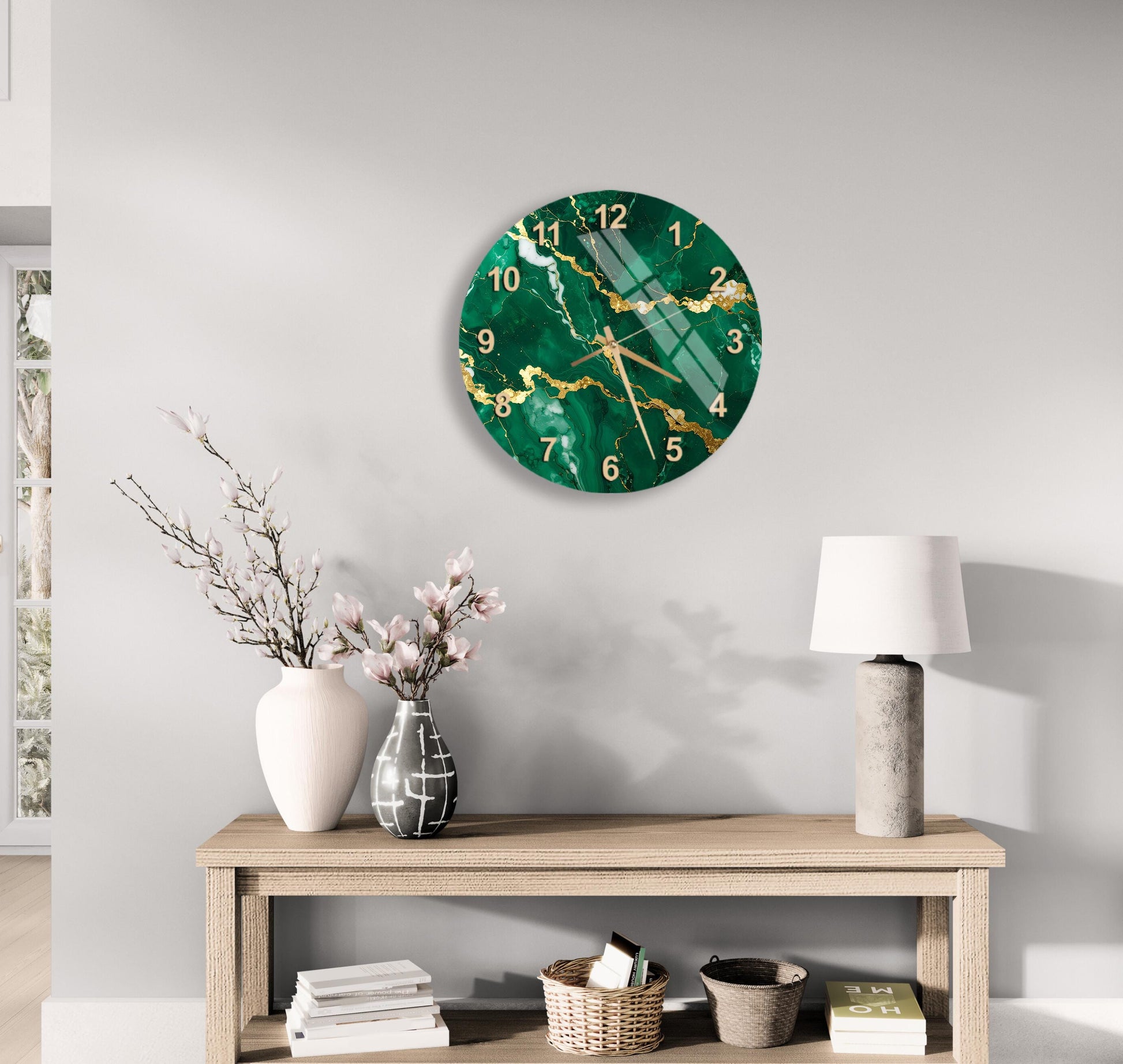 a modern living room with a large green marble clock hanging on the wall above a wooden table. The table has a lamp, a vase with flowers, and some books on it. The overall decor has a minimalist and elegant style.