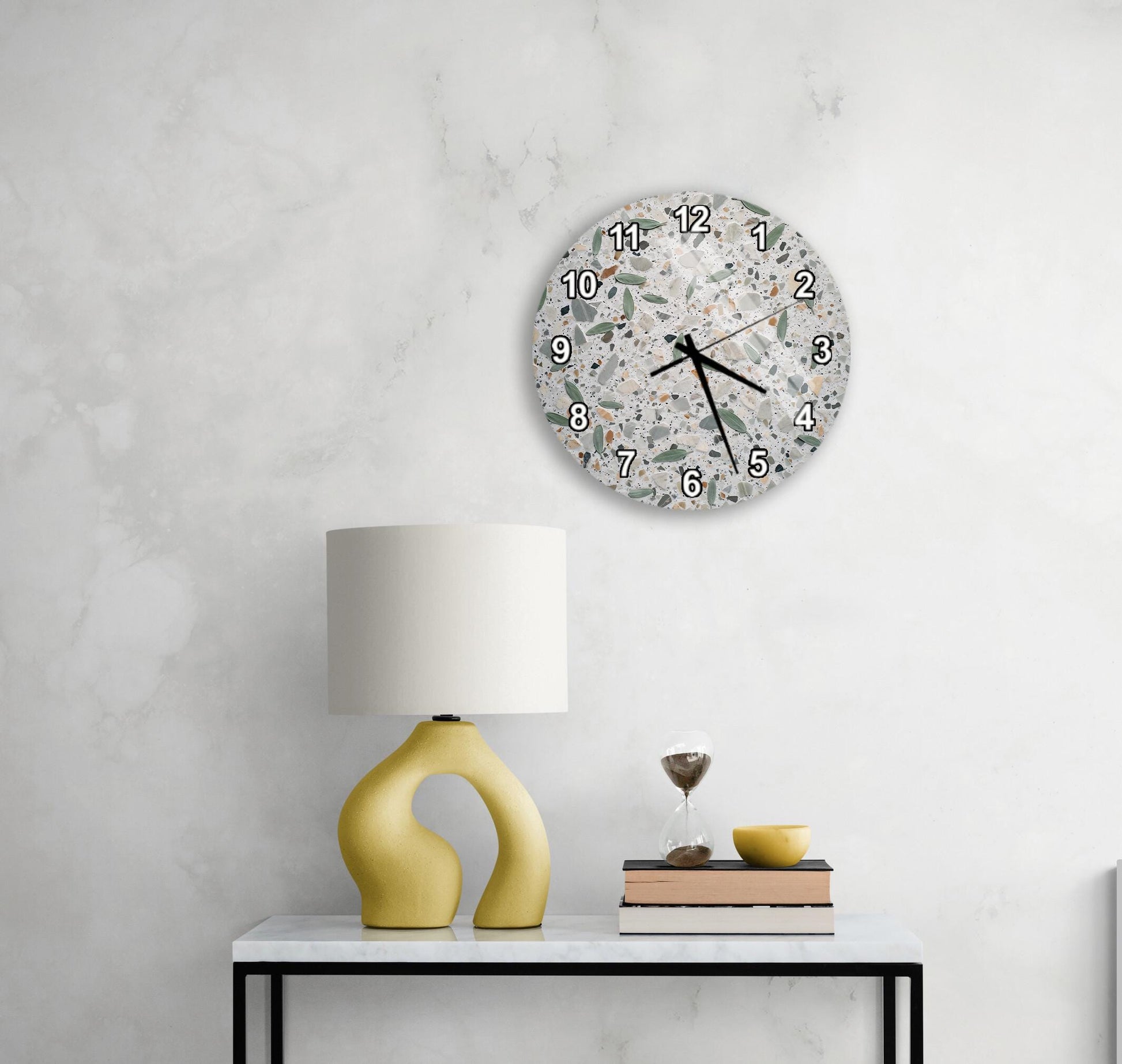 a modern, minimalist living space with a white marble wall, a round clock with a unique design, a yellow lamp with an unusual, curved base, and a small table with a stack of books and a glass of wine.