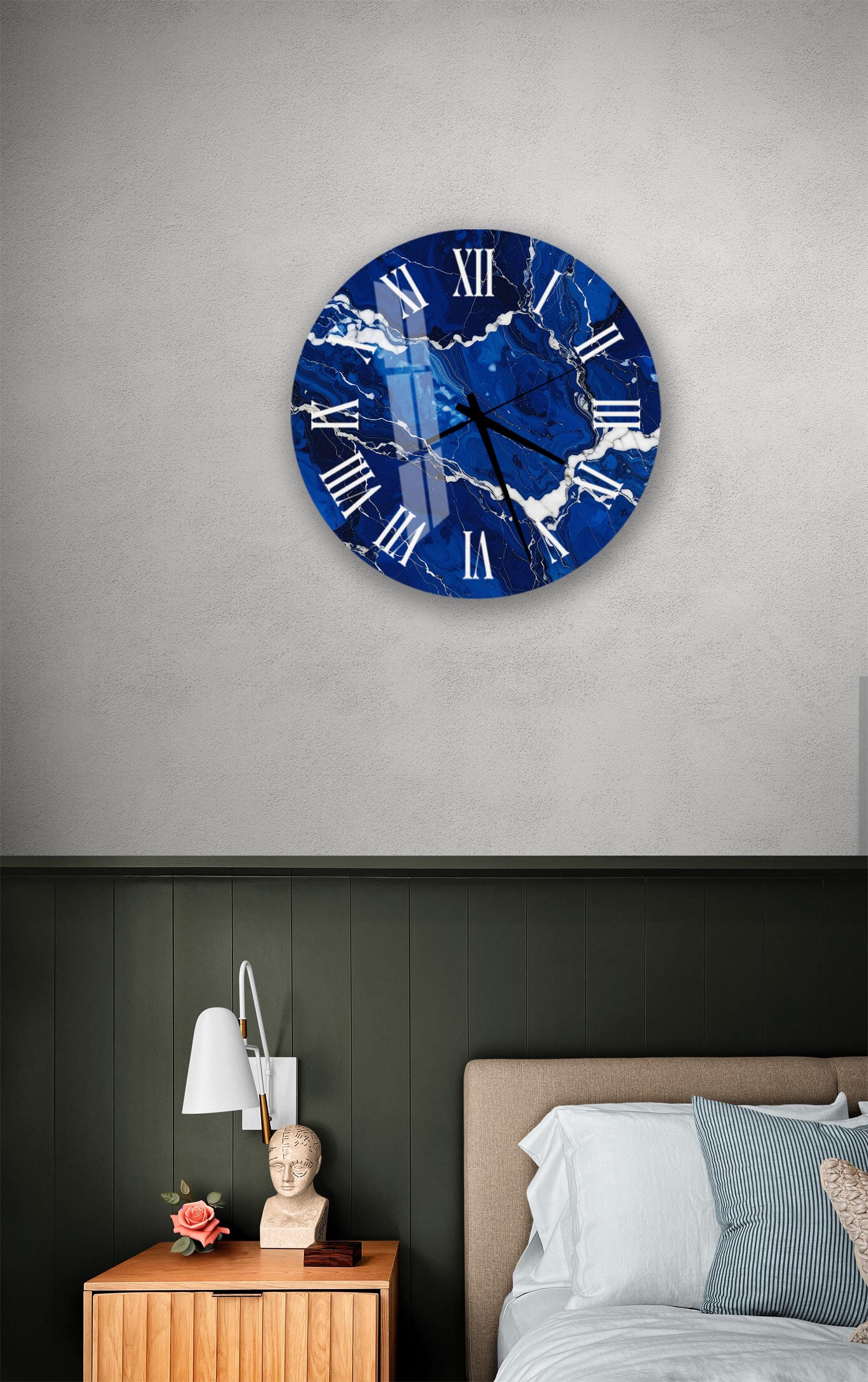 a bedroom setting with a large blue marble clock hanging on the wall above a bed. The clock has a white face with black Roman numerals. The room has a green wall, a wooden nightstand with a lamp, and a bed with white sheets.