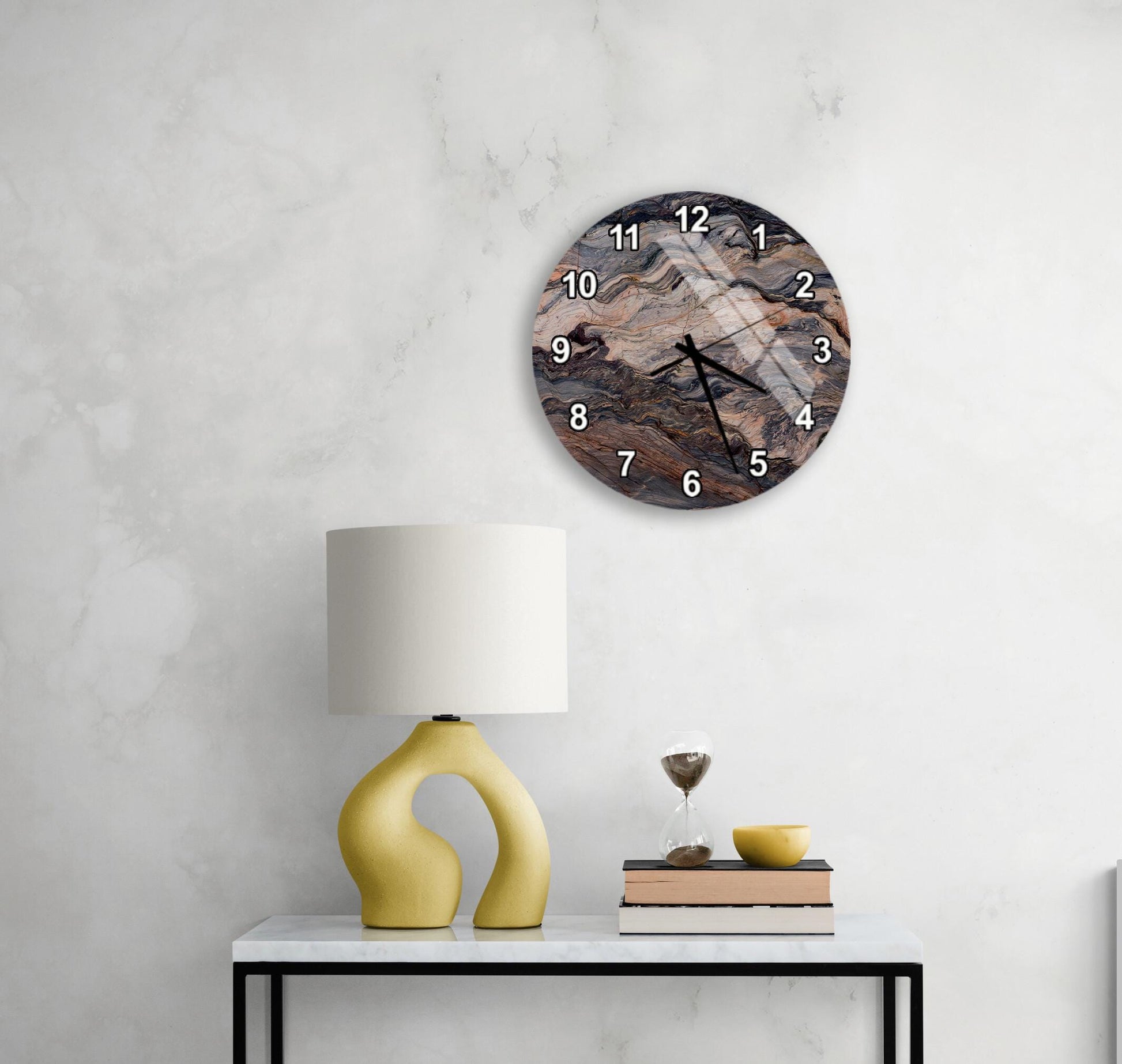 a modern living room with a white marble wall, a round wall clock with a unique design, a yellow lamp with a curved base, a stack of books, and a glass of wine on a white table.