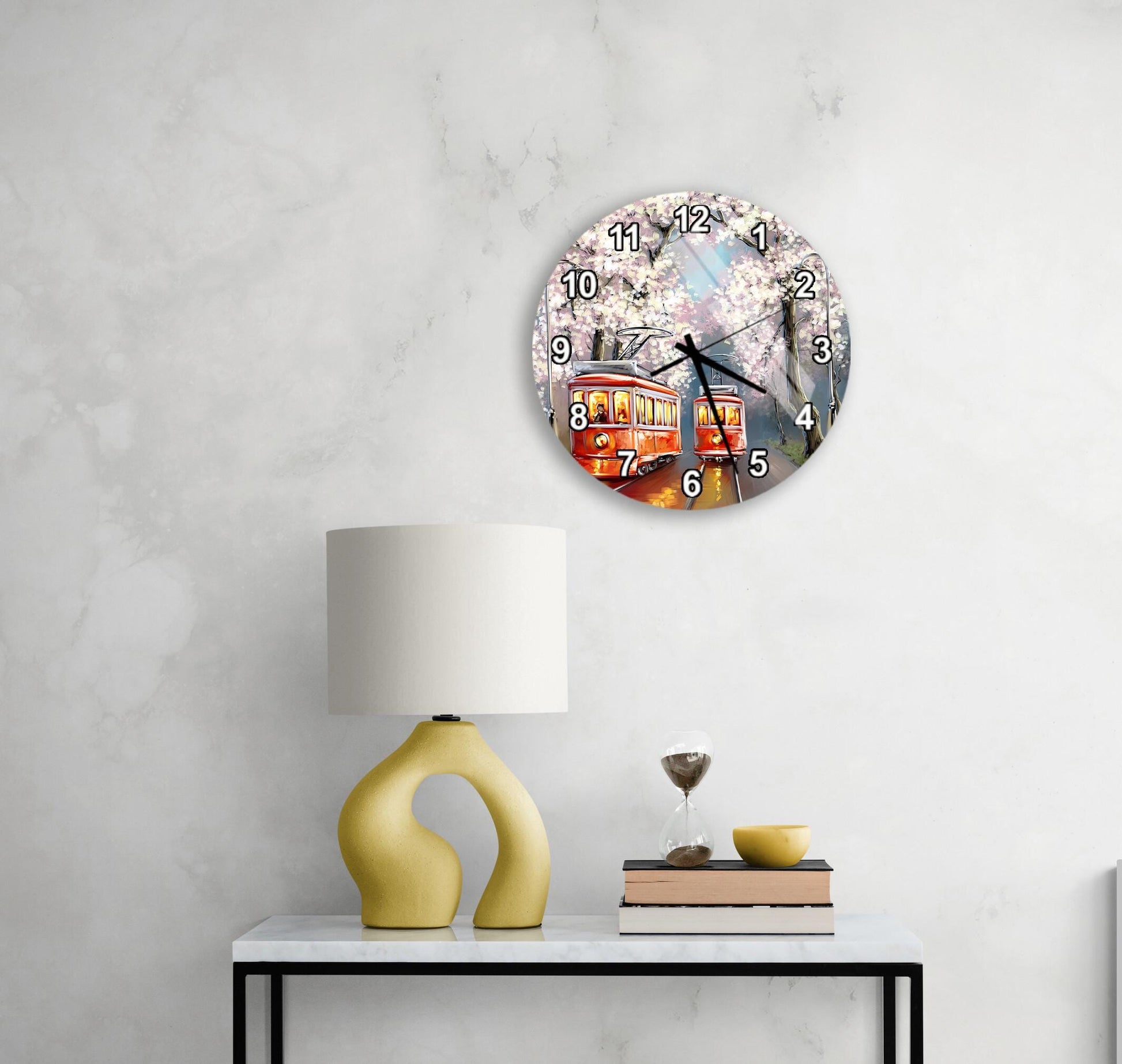 a wall clock with a trolley car design, a yellow lamp on a table, and a stack of books.