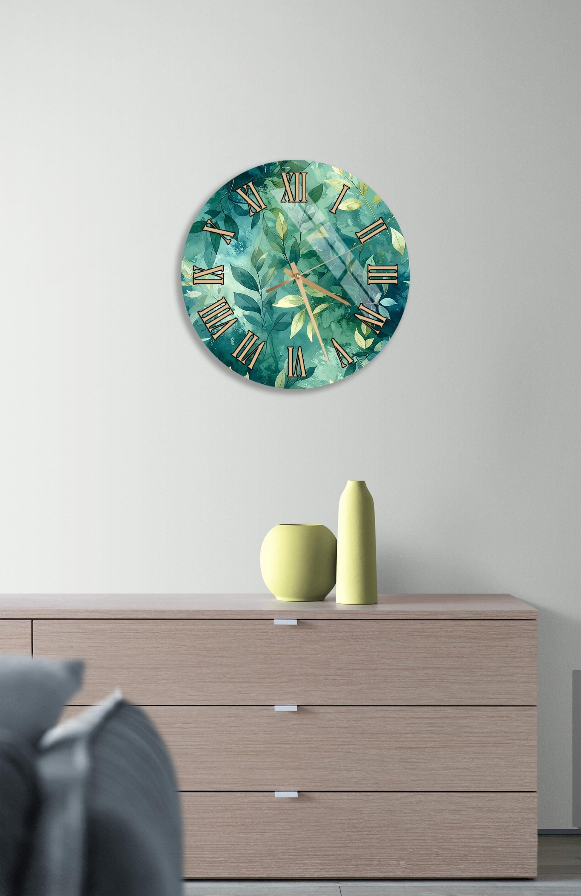 a wall clock with a green and white leaf design, mounted on a wall above a wooden dresser with three drawers.