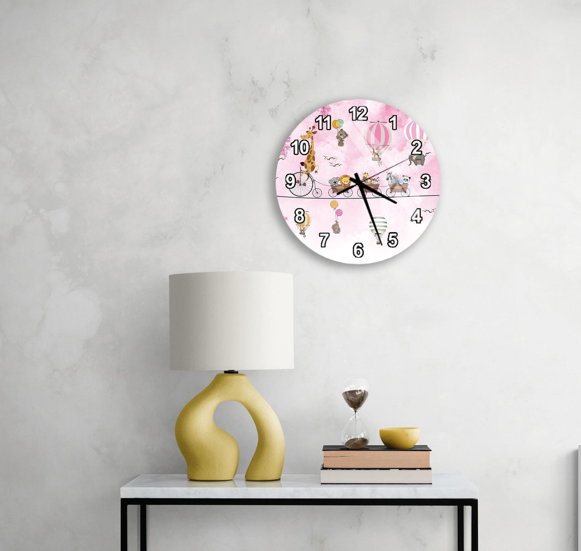 a pink wall clock with a cartoon character design, a yellow lamp on a white table, and a stack of books and a glass of water on the table.