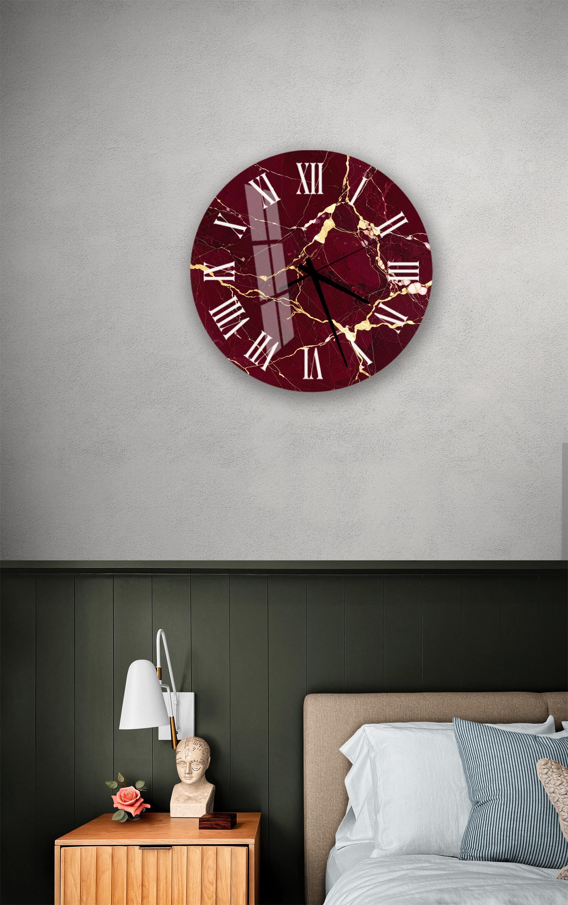 a bedroom setting with a large burgundy-colored clock hanging on the wall above a bed. The clock has a marble-like design and is positioned at eye level. The room also includes a nightstand with a lamp and a small statue or bust.