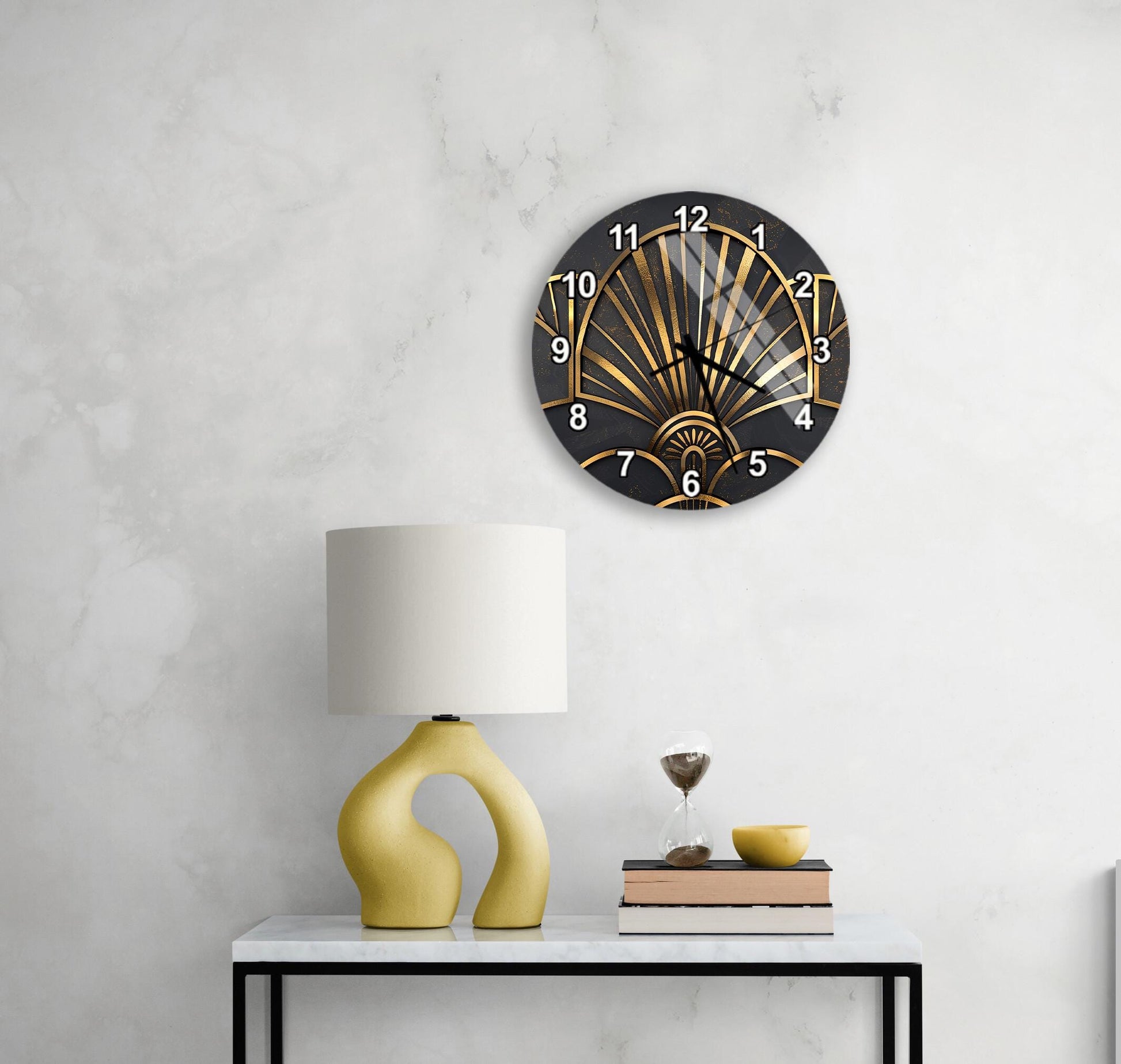 a modern black and gold wall clock with a black face and gold hands, mounted on a white wall above a white table with a yellow lamp and a stack of books.