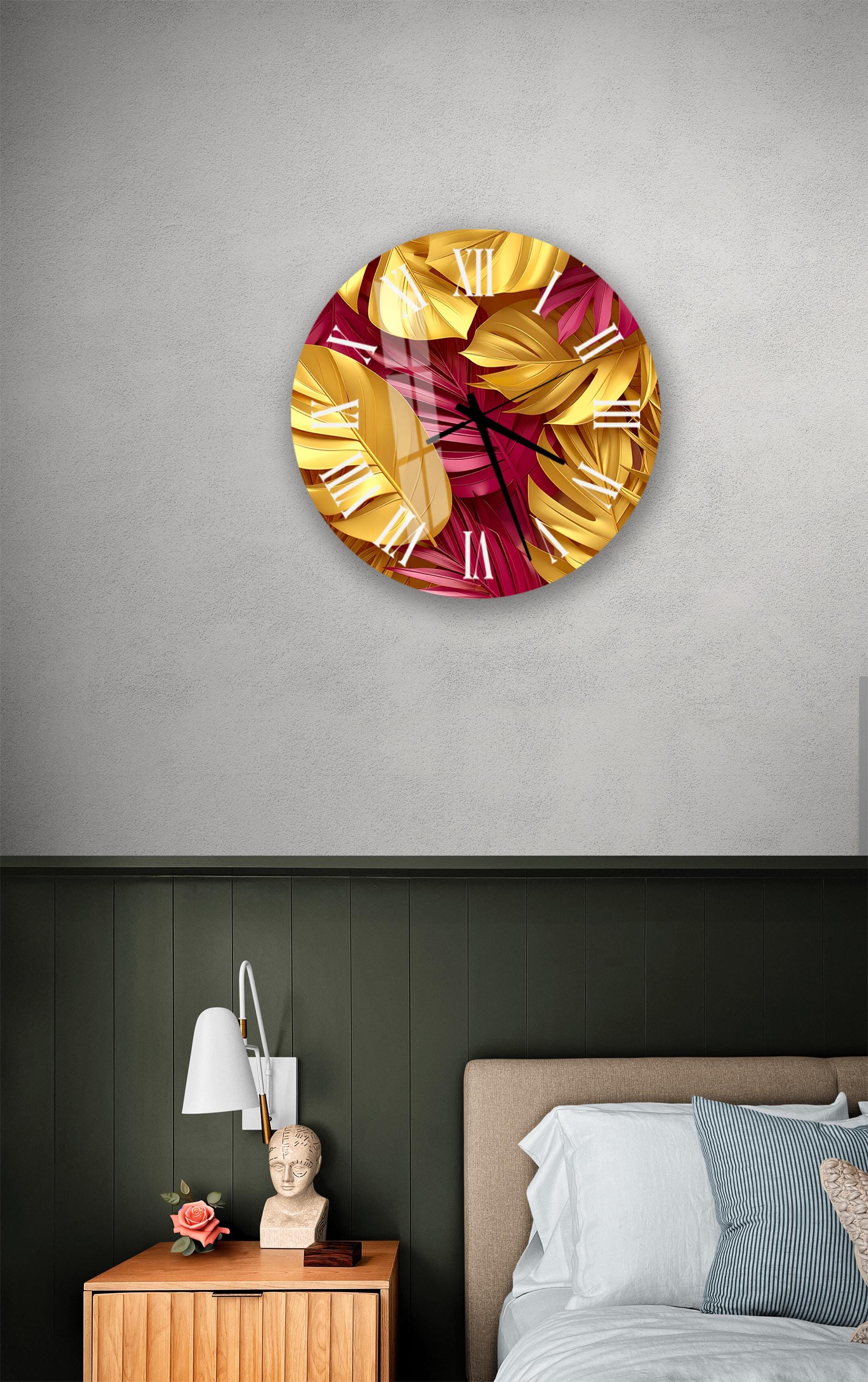 a bedroom setting with a large wall clock displaying a vibrant design of yellow and red leaves. The clock is mounted on a gray wall above a bed with a white headboard. The room also includes a nightstand with a lamp and a small statue, creating a cozy and stylish atmosphere.