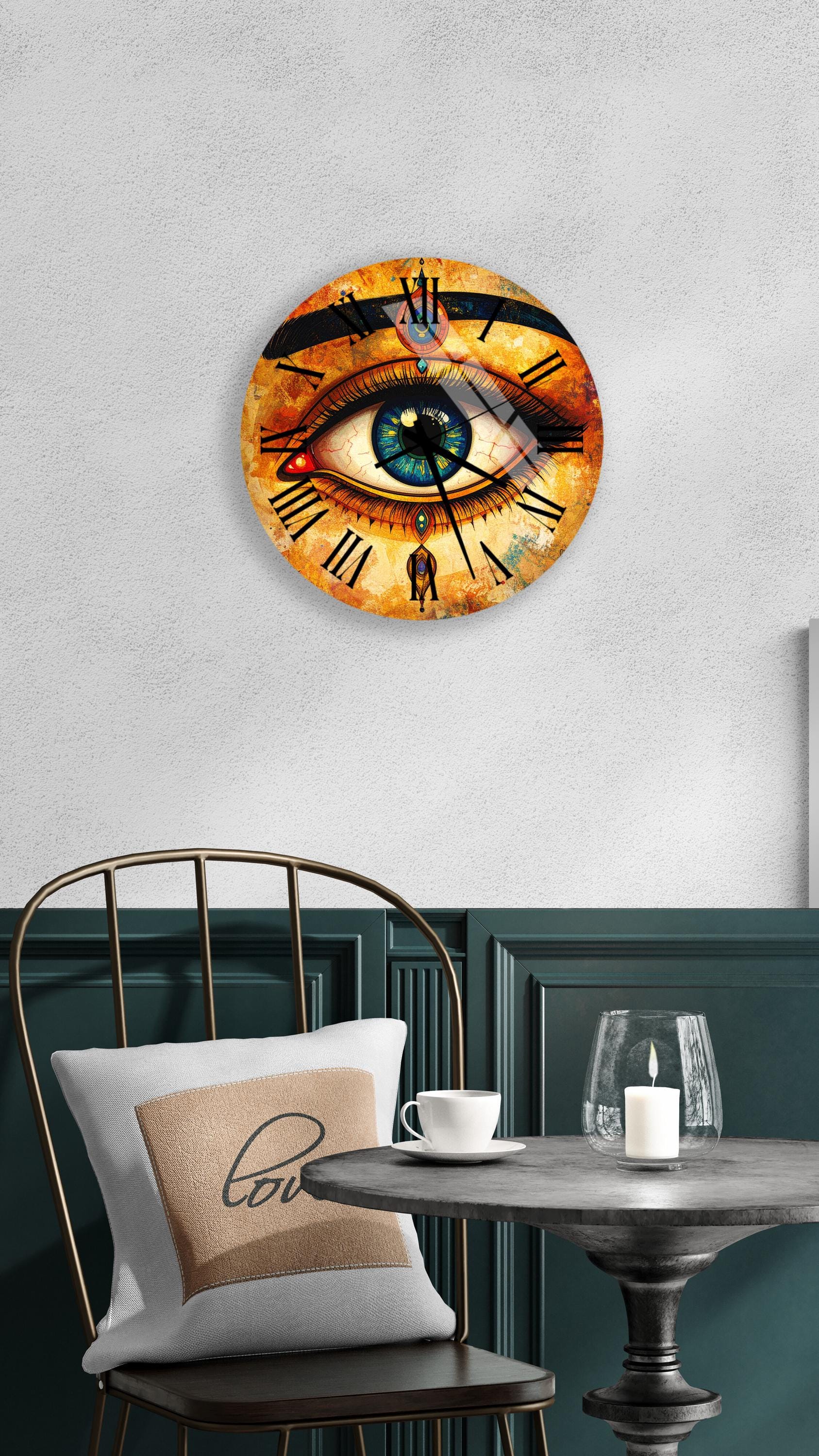 a wall clock with an eye design, a white table with a candle and a cup, and a chair with a pillow on it.