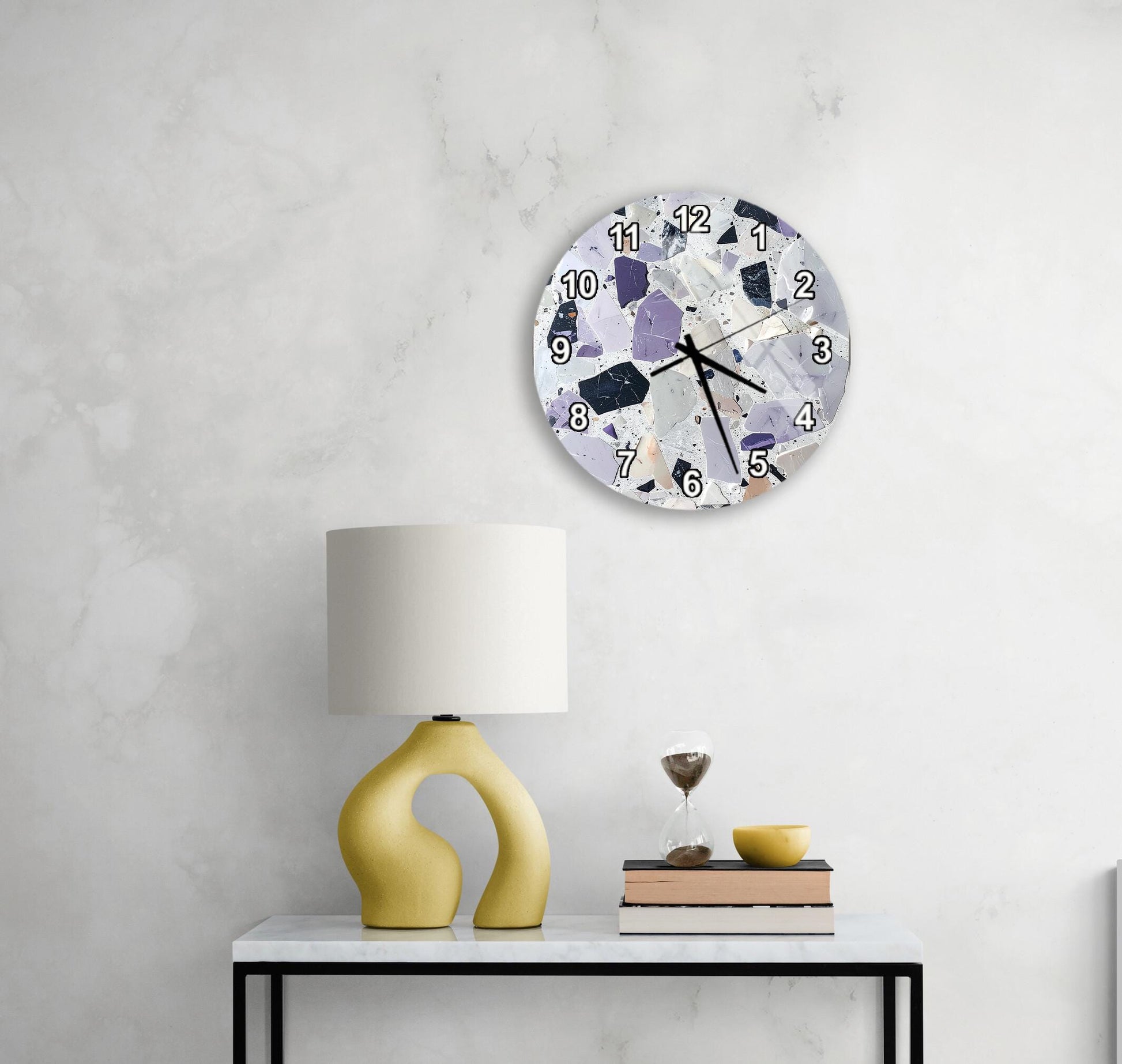 a modern, minimalist living space with a white marble wall, a round clock with a unique design, a yellow lamp with an unusual, curved base, and a small table with a book and a glass of water.