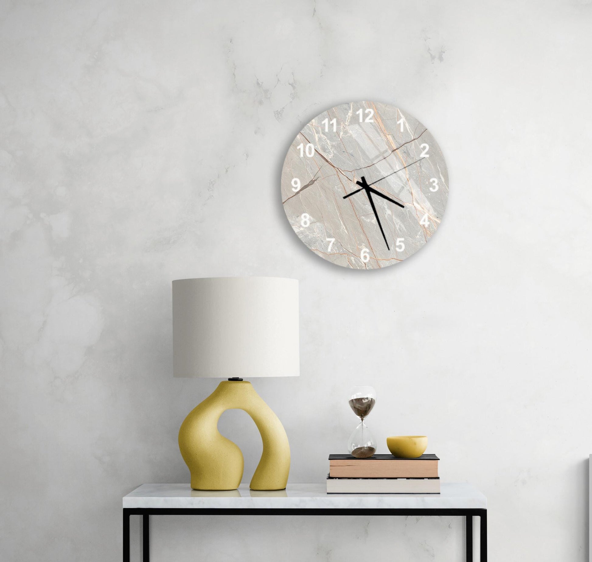 a modern living room with a white marble wall, a round clock with a marble design, a yellow lamp with a unique curved base, a stack of books, and a glass of wine on a white table.
