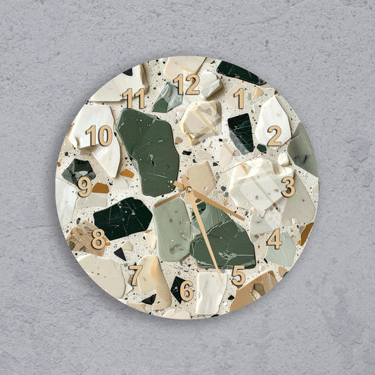 A round wall clock with a mosaic design made up of various colored tiles, including shades of green, white, and beige.