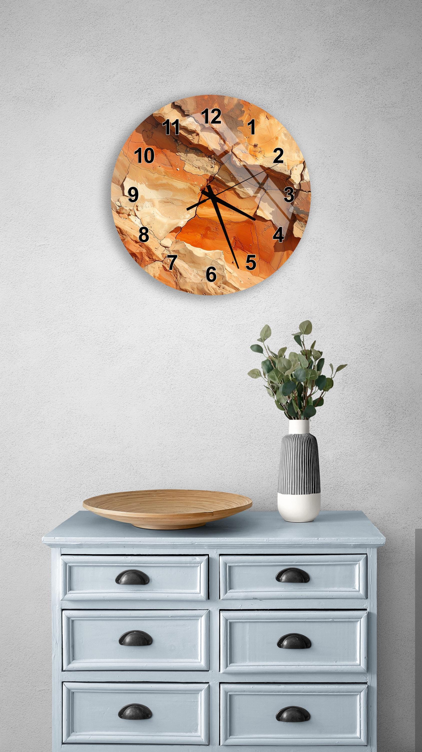 a wall clock with a unique orange and brown abstract design, mounted on a wall above a light blue dresser with six drawers. The dresser also has a vase with greenery on it, and there is a wooden plate on top of the dresser.