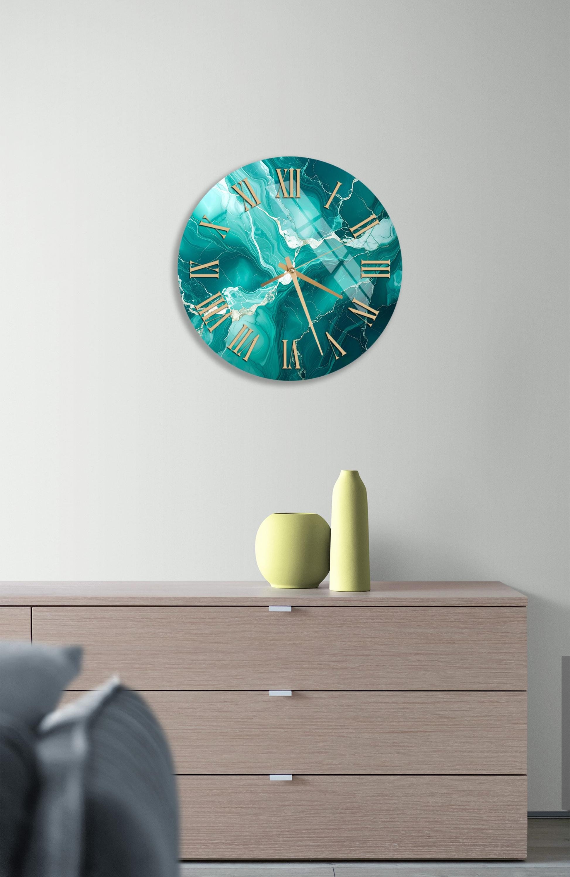 a modern living room with a large turquoise marble clock hanging on the wall above a wooden dresser. The dresser has three drawers and a vase on top.