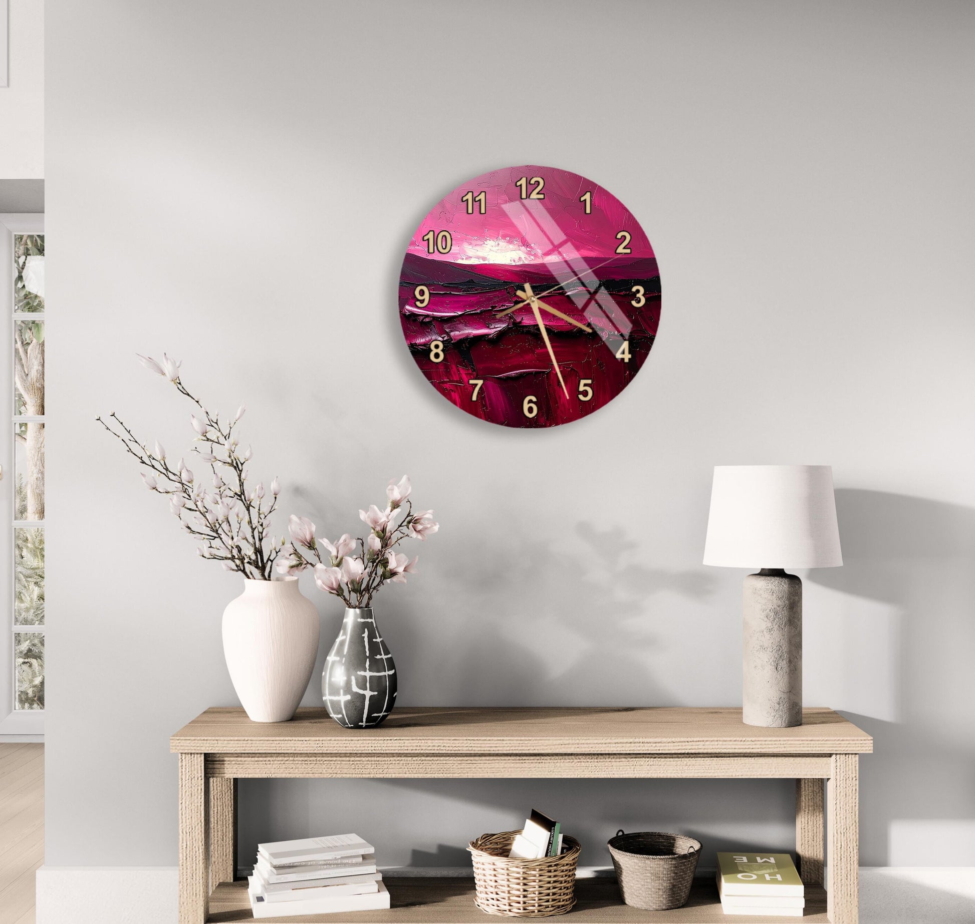 a wall clock with a pink and purple design, a wooden table with a lamp, a vase with flowers, and some books on a shelf.