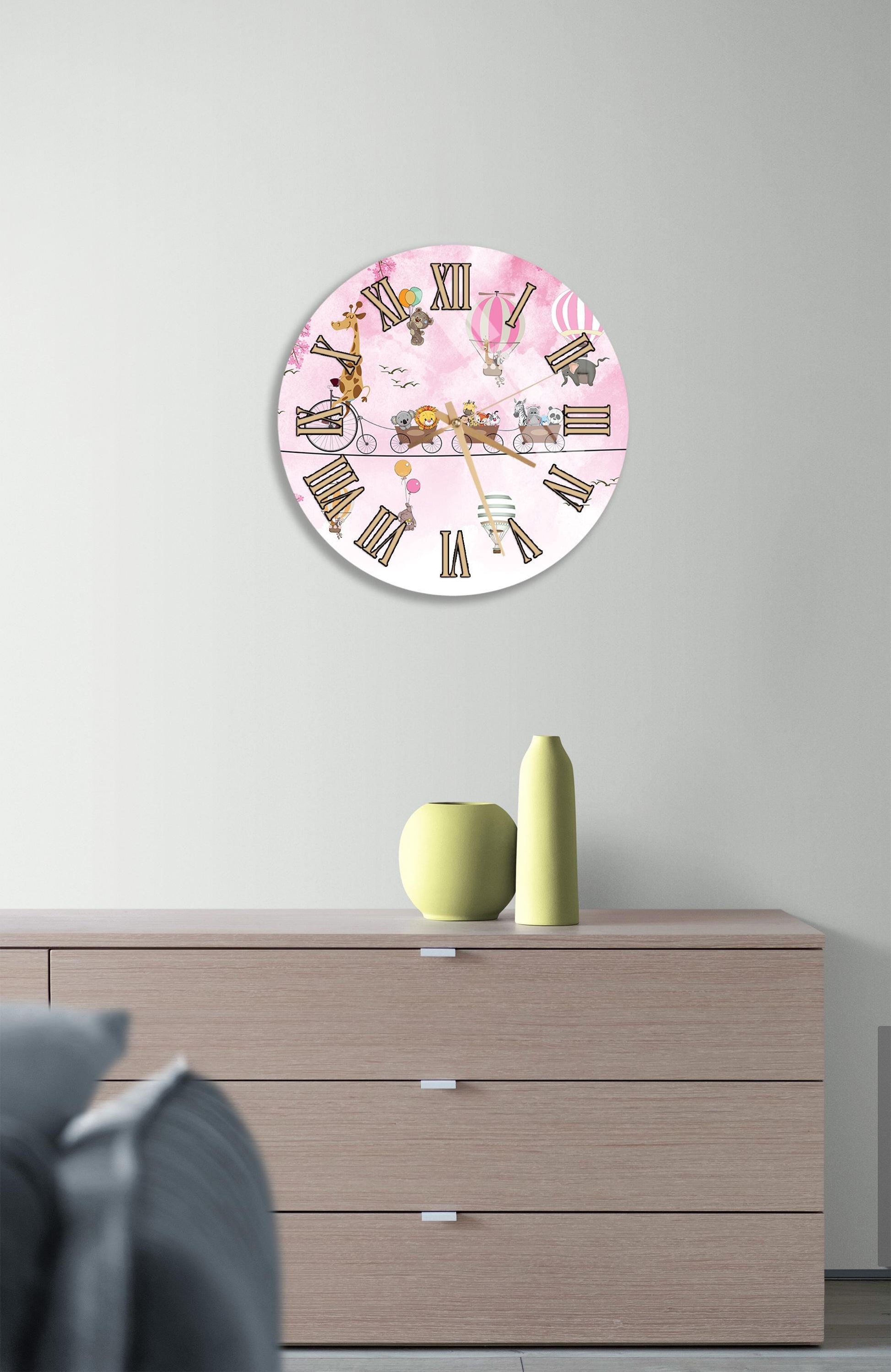 a round clock with a pink background and Roman numerals, hanging on a wall above a wooden dresser.