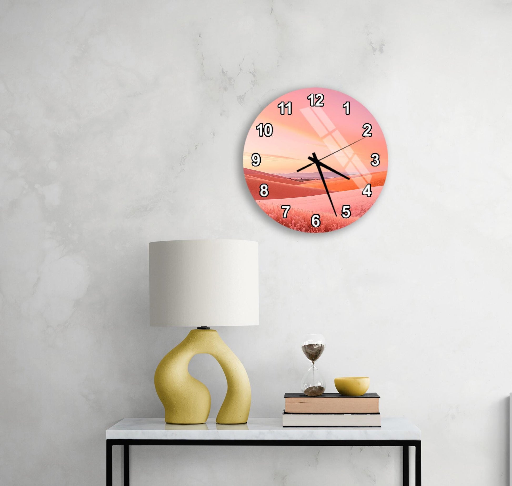 a wall clock with a sunset design, a yellow lamp, a stack of books, and a glass of wine on a white table.