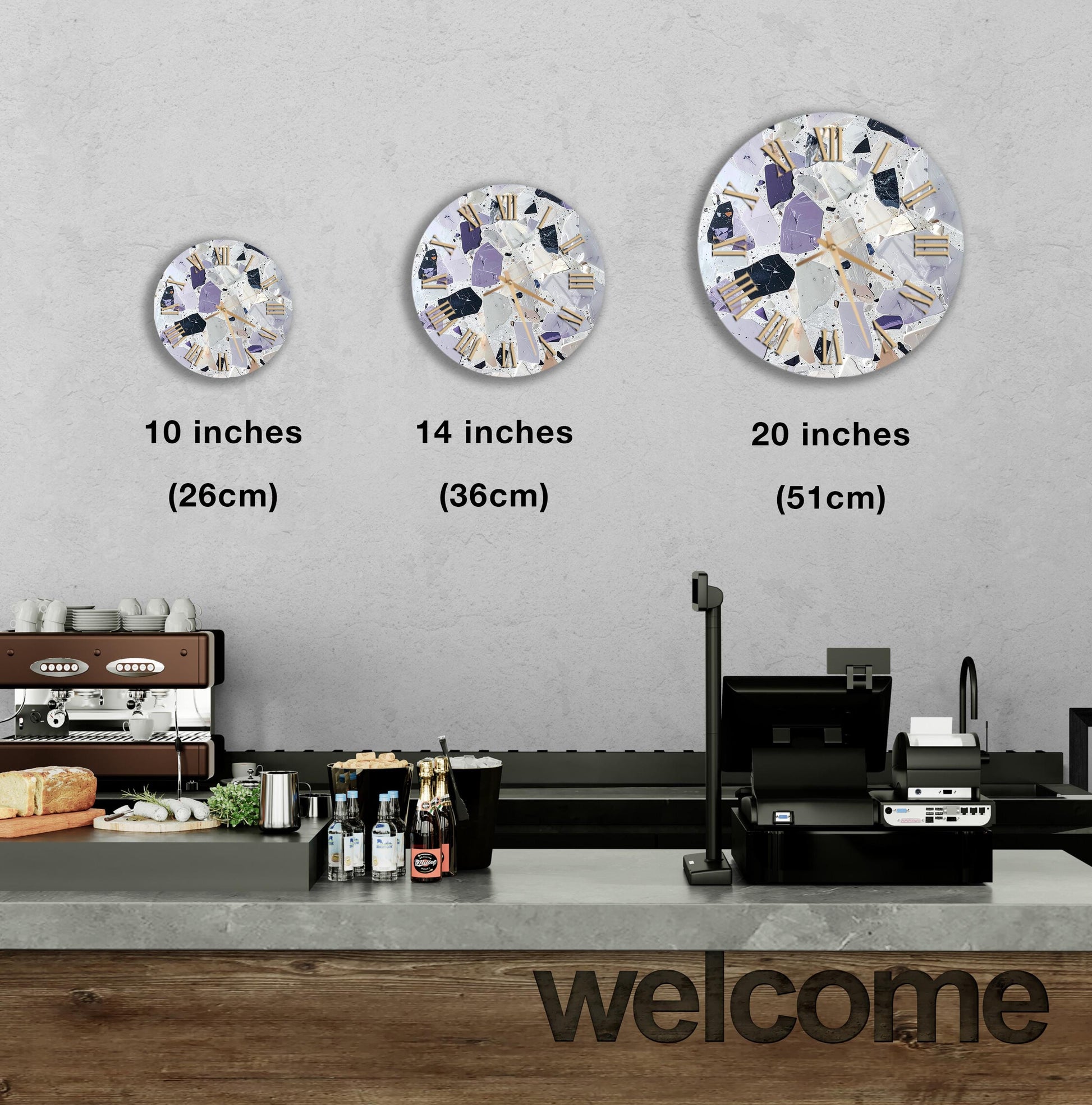 a counter in a restaurant with a "welcome" sign, and three different sizes of wall clocks hanging above it.
