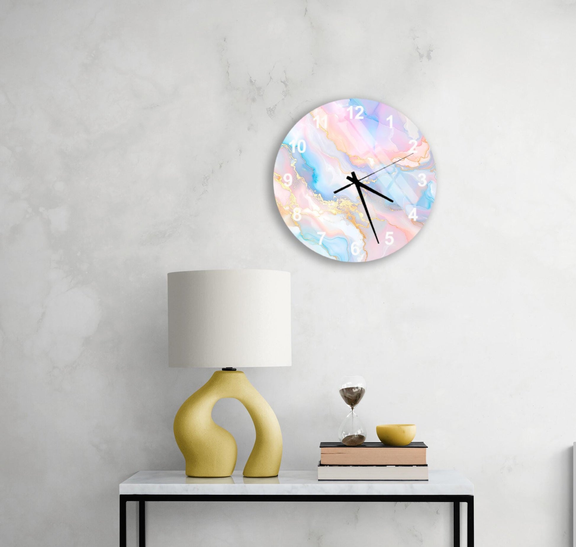 a white wall with a round clock displaying a colorful abstract design, a yellow lamp on a white table, and a stack of books and a glass of water on the table.
