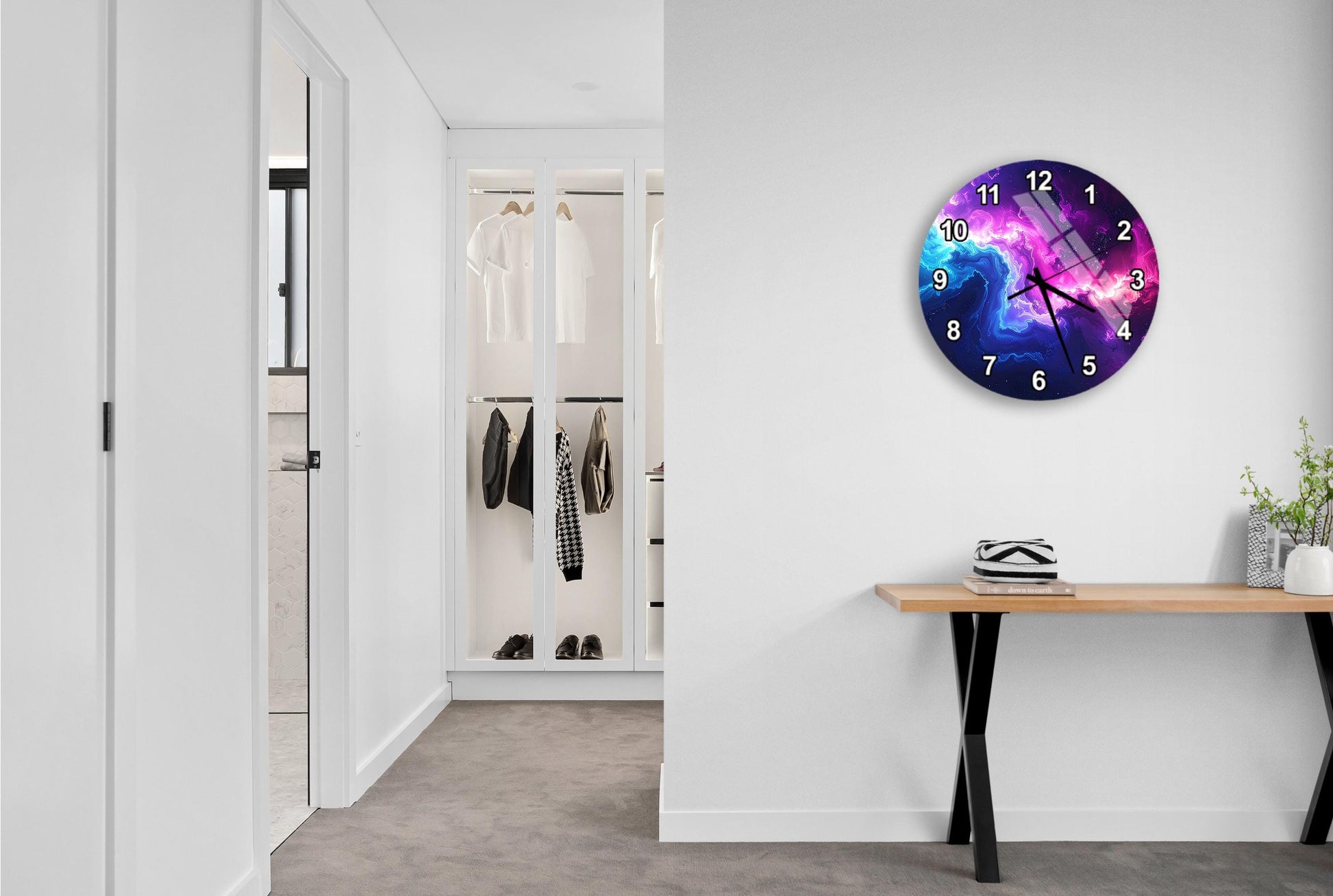 a hallway with a wall clock displaying a colorful galaxy design. The hallway is clean and well-lit, with a wooden table and a plant on the floor.