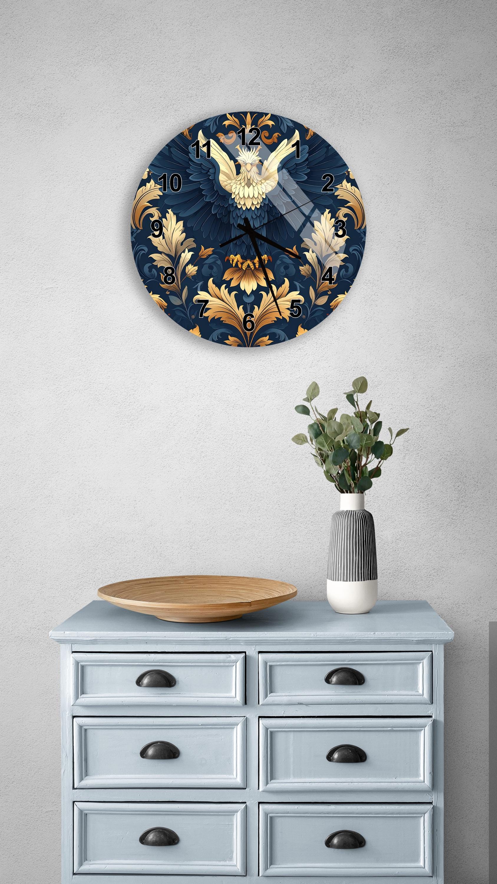 a wall clock with a blue and gold design, mounted on a wall above a light blue dresser with six drawers. The dresser also has a vase with greenery and a wooden bowl on it.