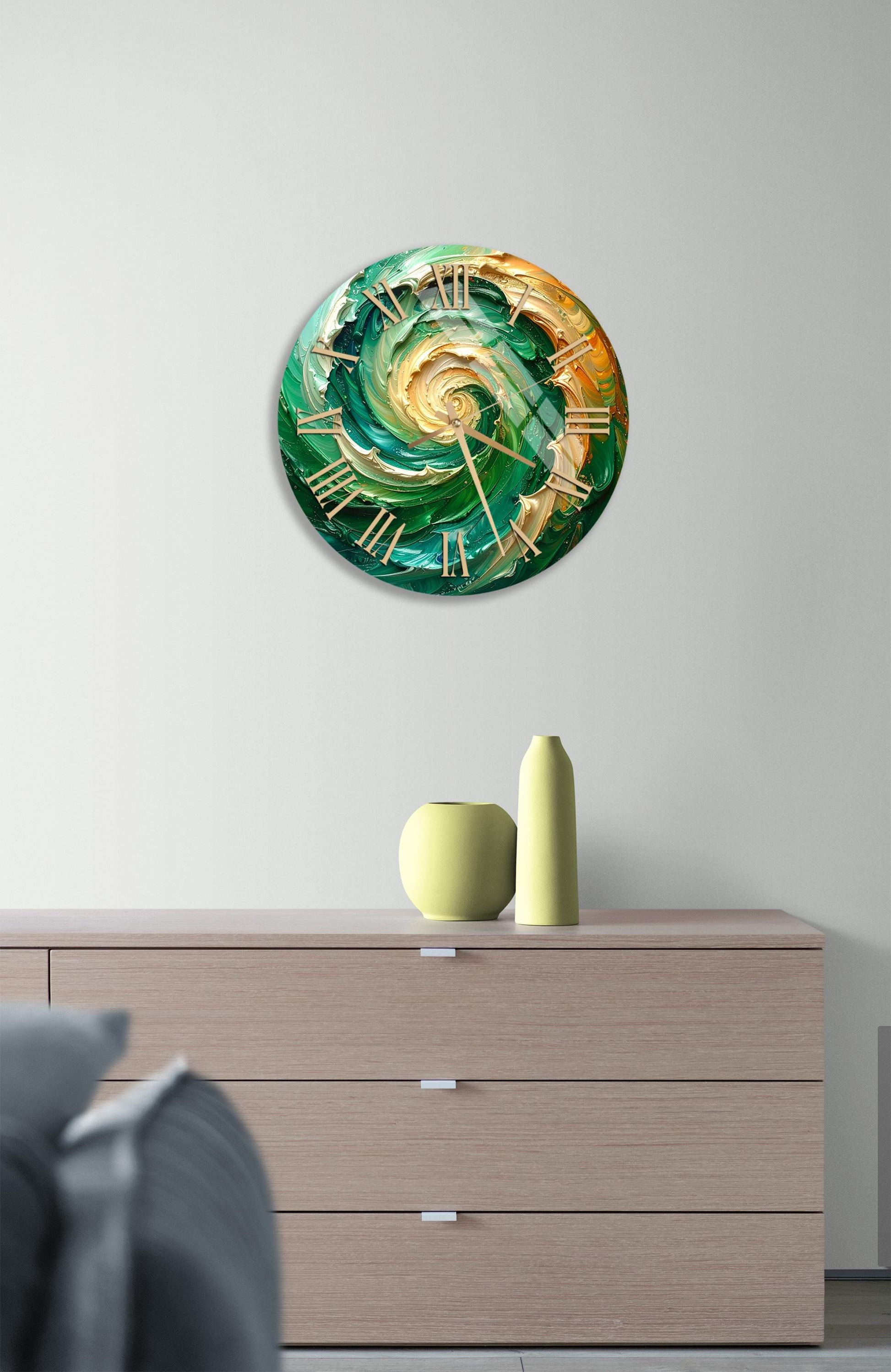a modern clock with a green and gold design, mounted on a wall above a wooden dresser with three drawers.