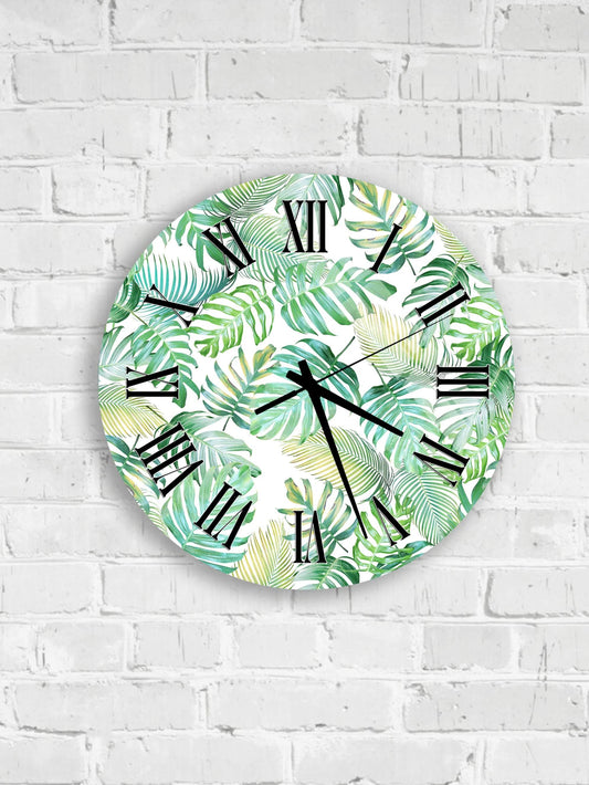 A round wall clock with a tropical leaf pattern on its face is mounted on a white brick wall.